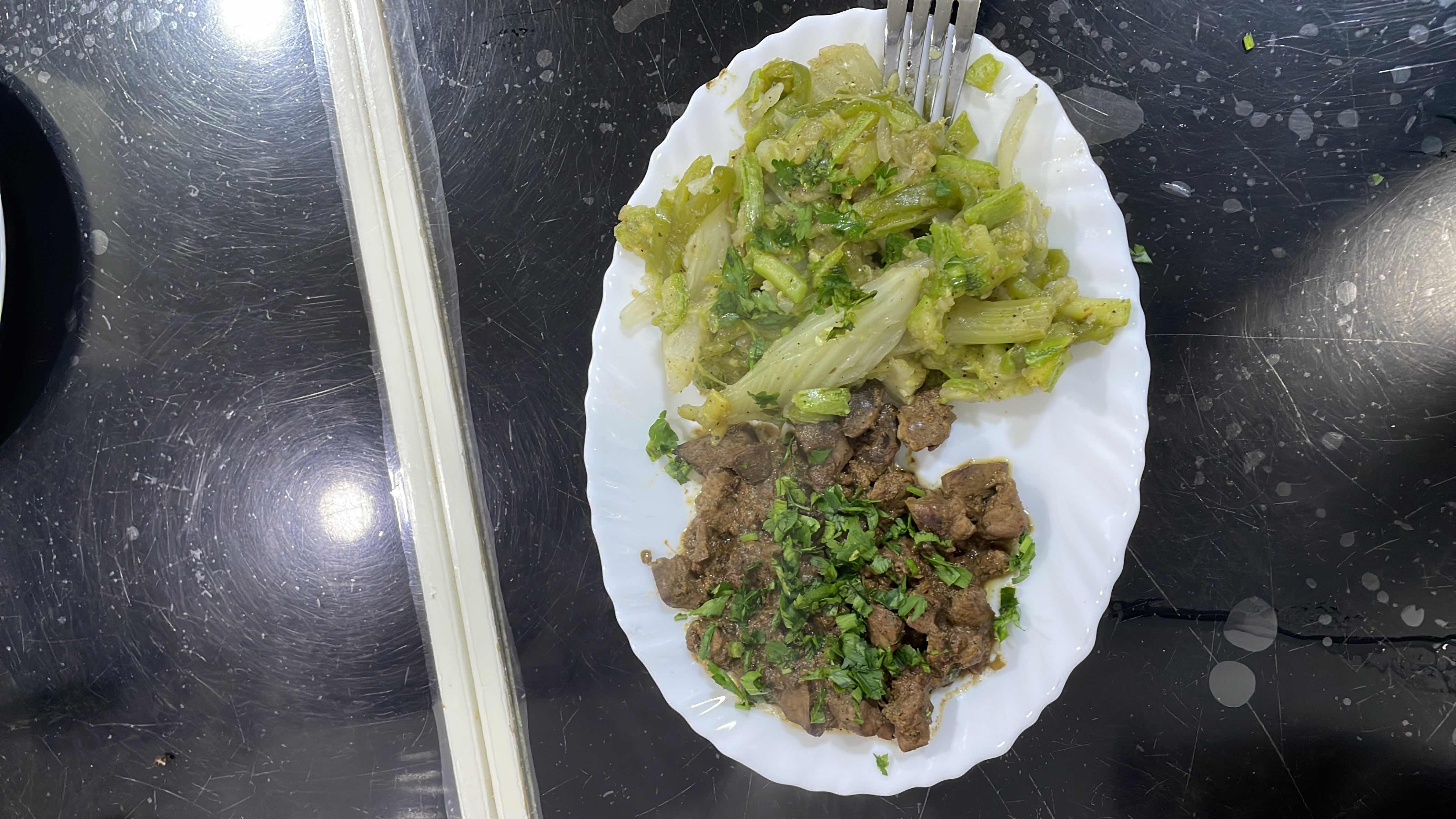 A plate of cooked beef liver garnished with cilantro, served alongside sautéed lettuce.