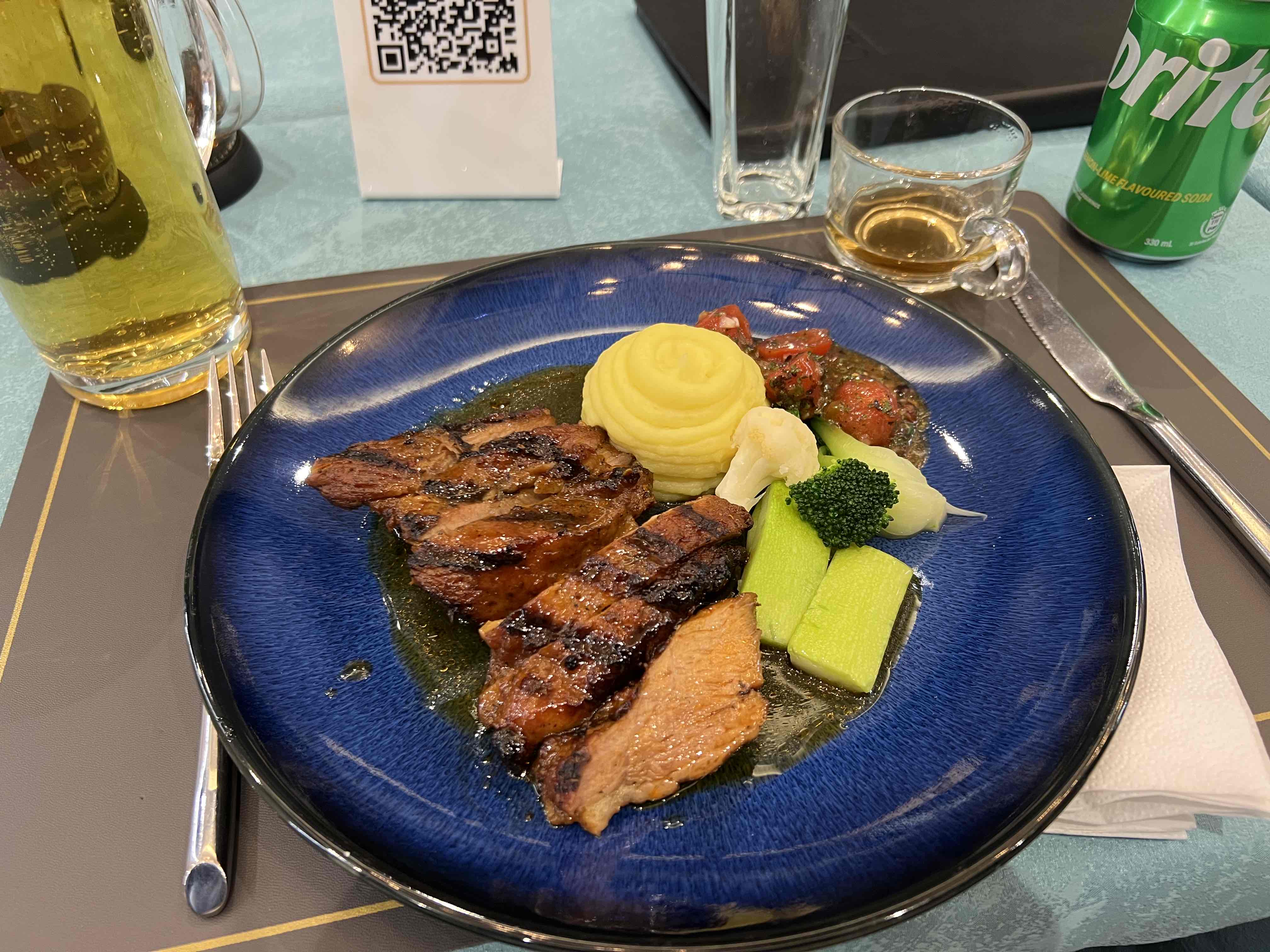 A balanced meal consisting of grilled meat, mashed potatoes, steamed vegetables, and a light sauce, served with beverages.