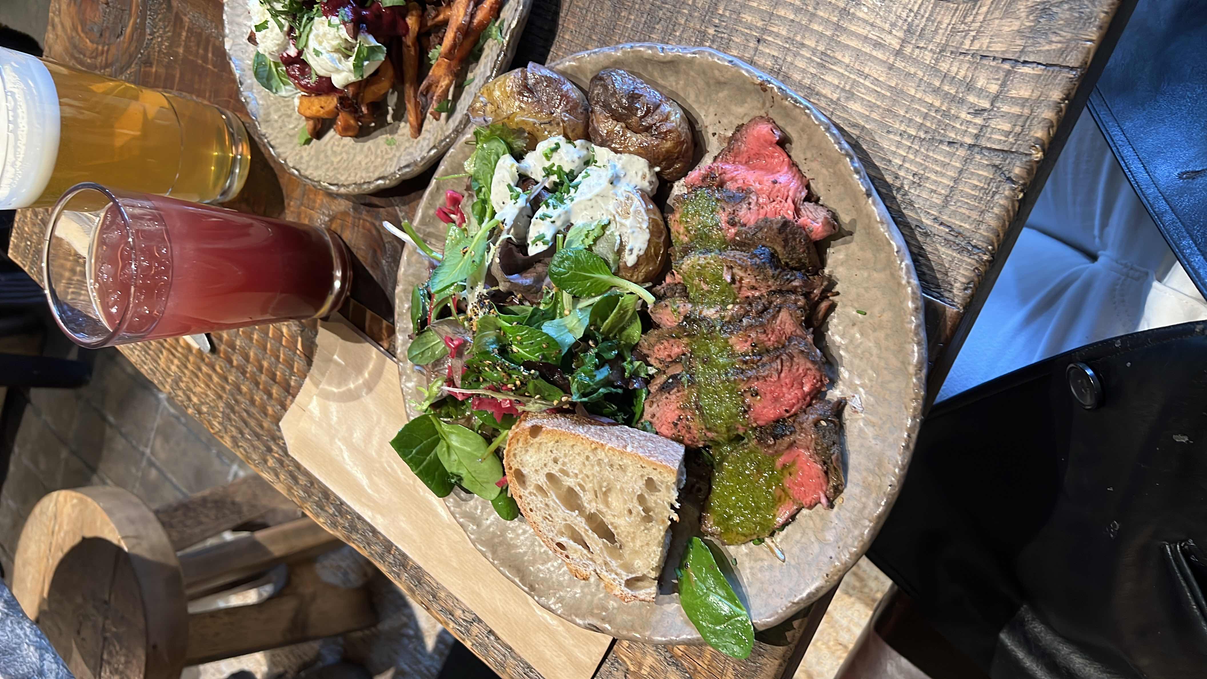 A balanced meal featuring steak with chimichurri sauce, roasted potatoes, mixed greens, and a slice of bread.