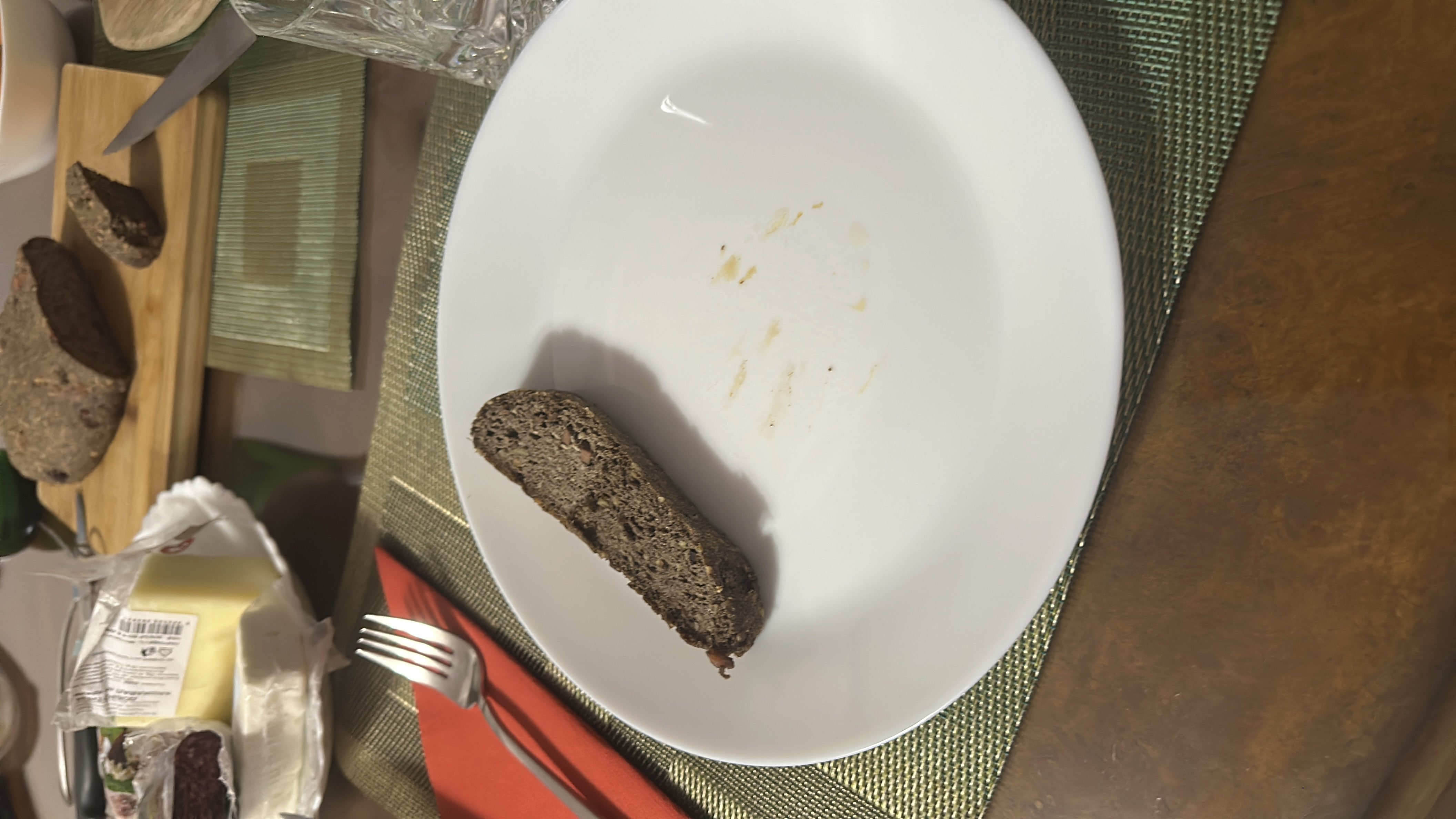 Two slices of keto flat seed bread made with flax seed and sunflower seeds, accompanied by cheese and other low-carb items in the background.