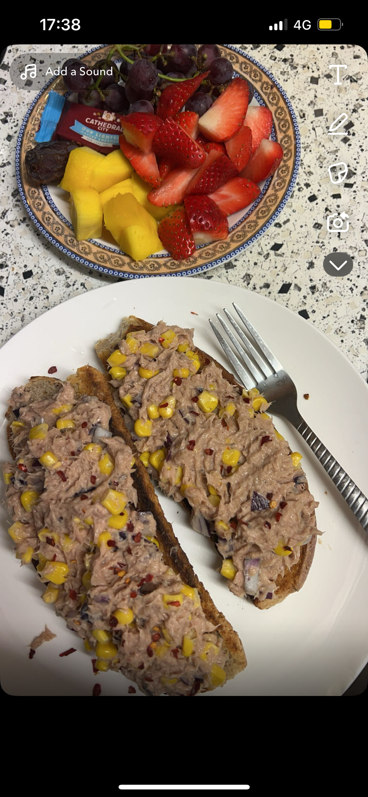 A balanced meal consisting of tuna and corn on whole grain bread, served with a side of fresh fruits including strawberries, mango, and grapes.
