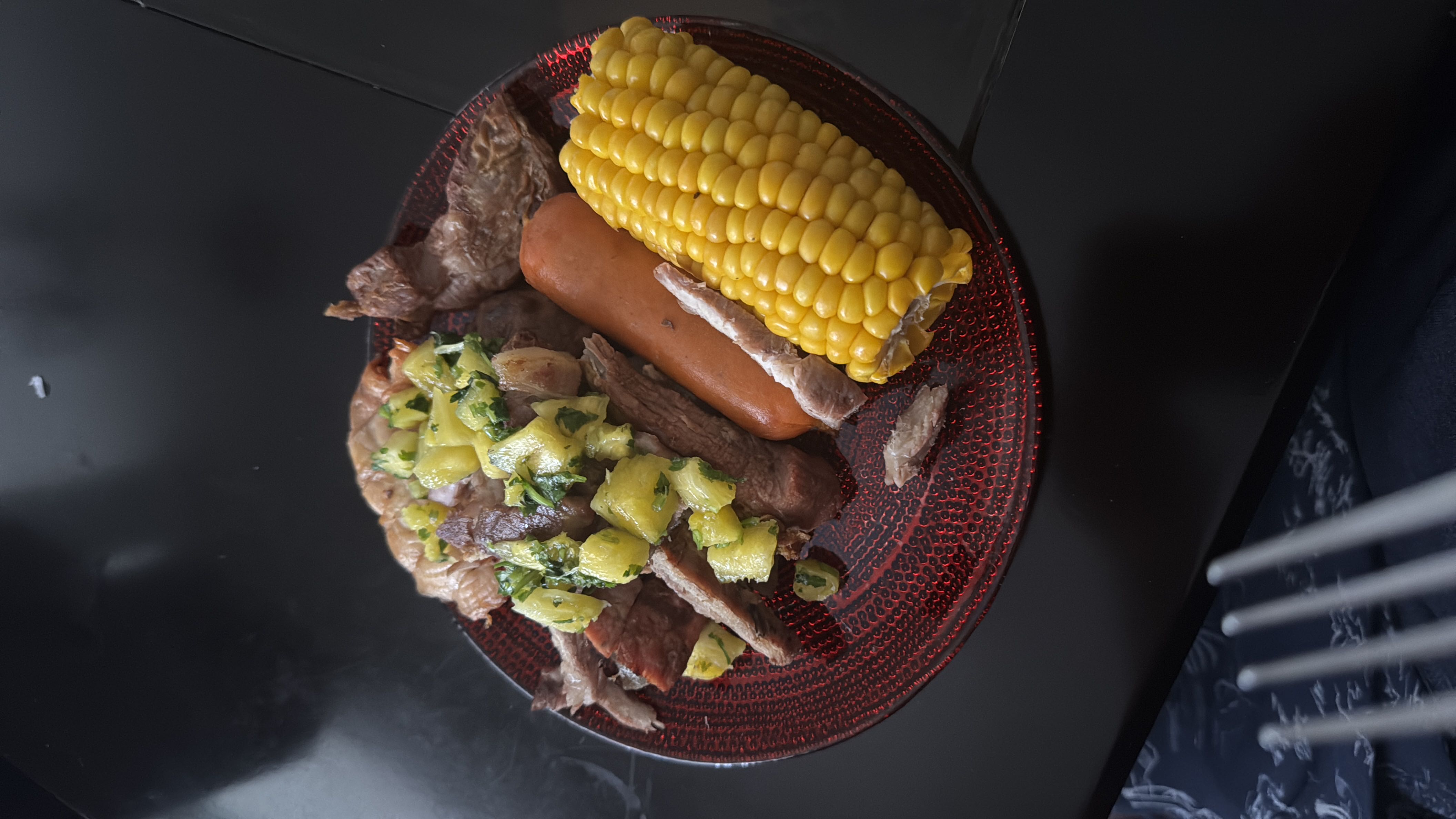 A balanced meal consisting of grilled beef, corn on the cob, and sausage, garnished with a pineapple salsa.