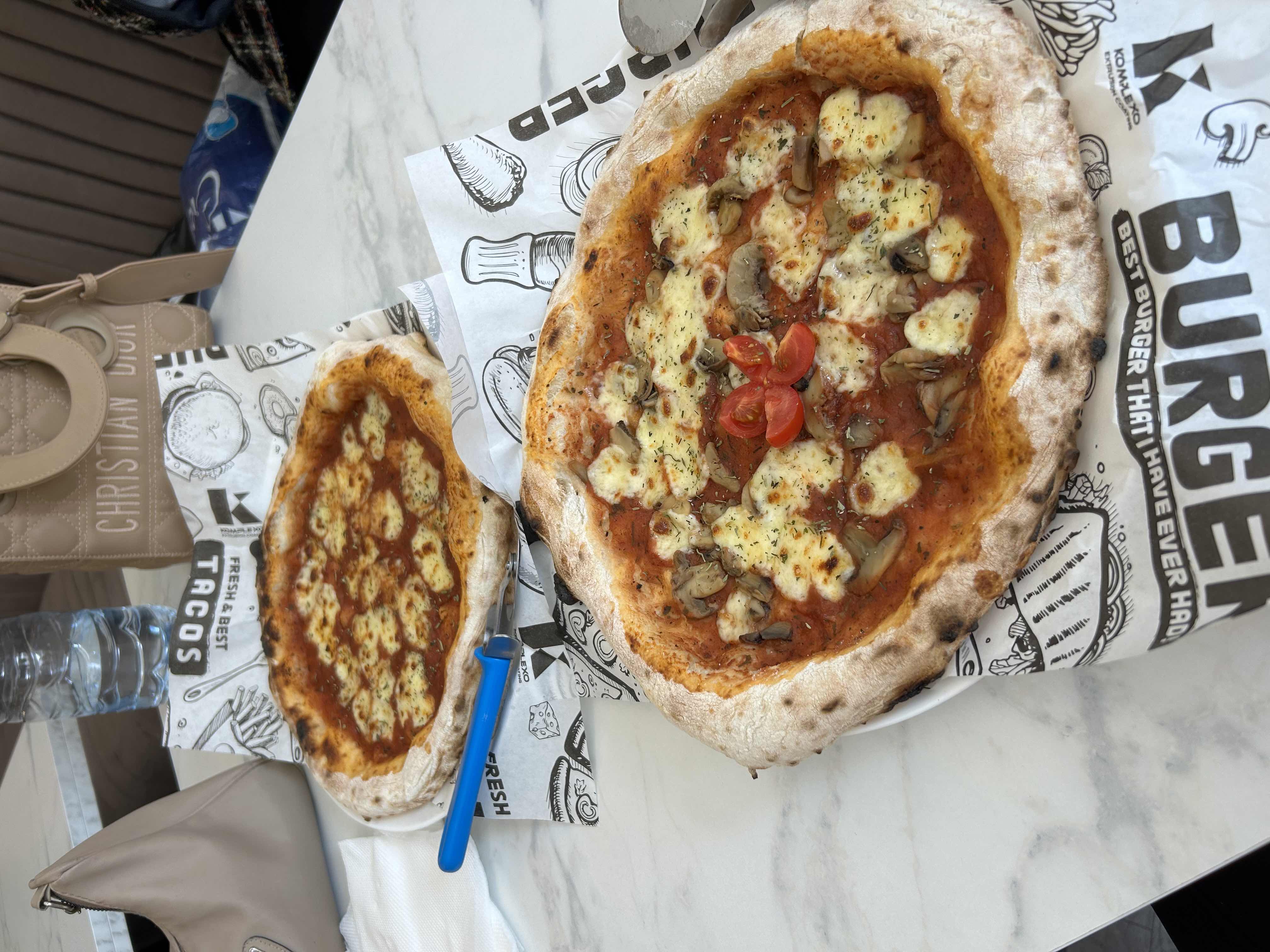 The image shows two pizzas with toppings including cheese, tomato sauce, and mushrooms, served on a thin crust.