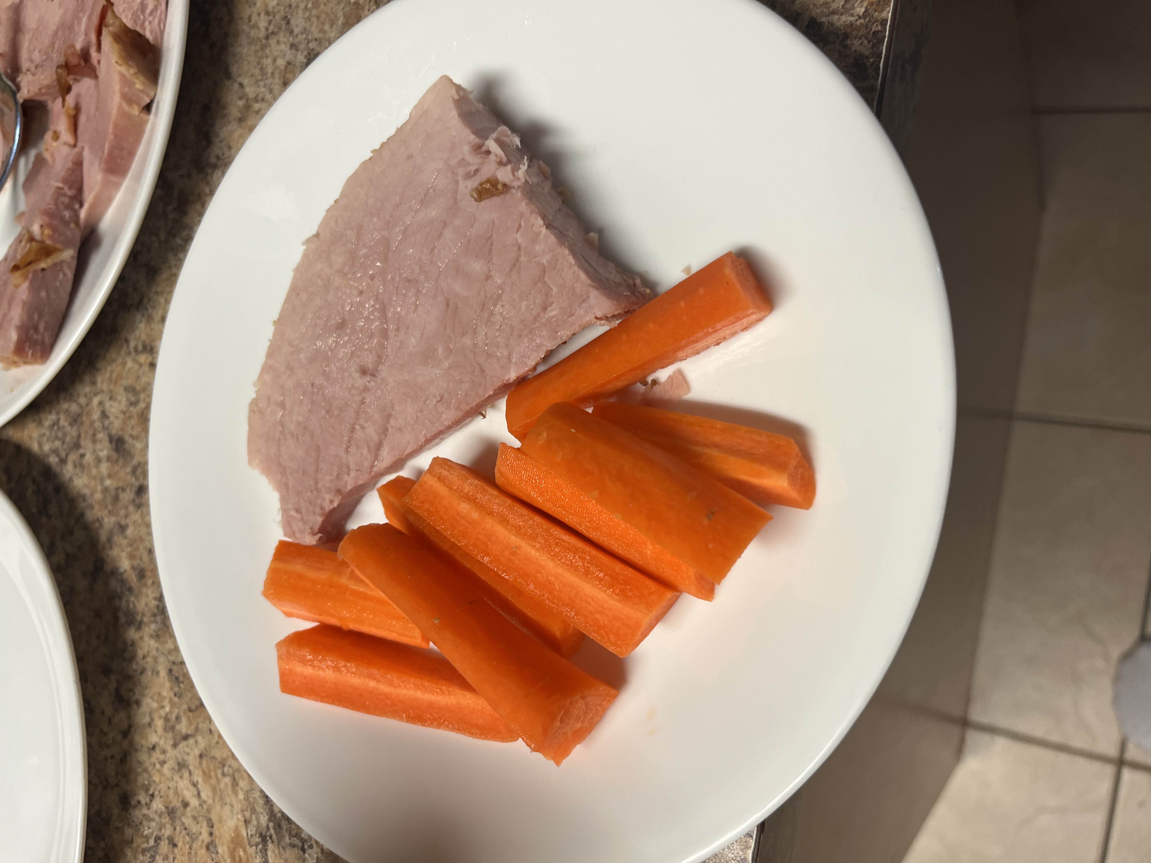 A plate containing a serving of ham and fresh carrot sticks, providing a balanced mix of protein and carbohydrates.