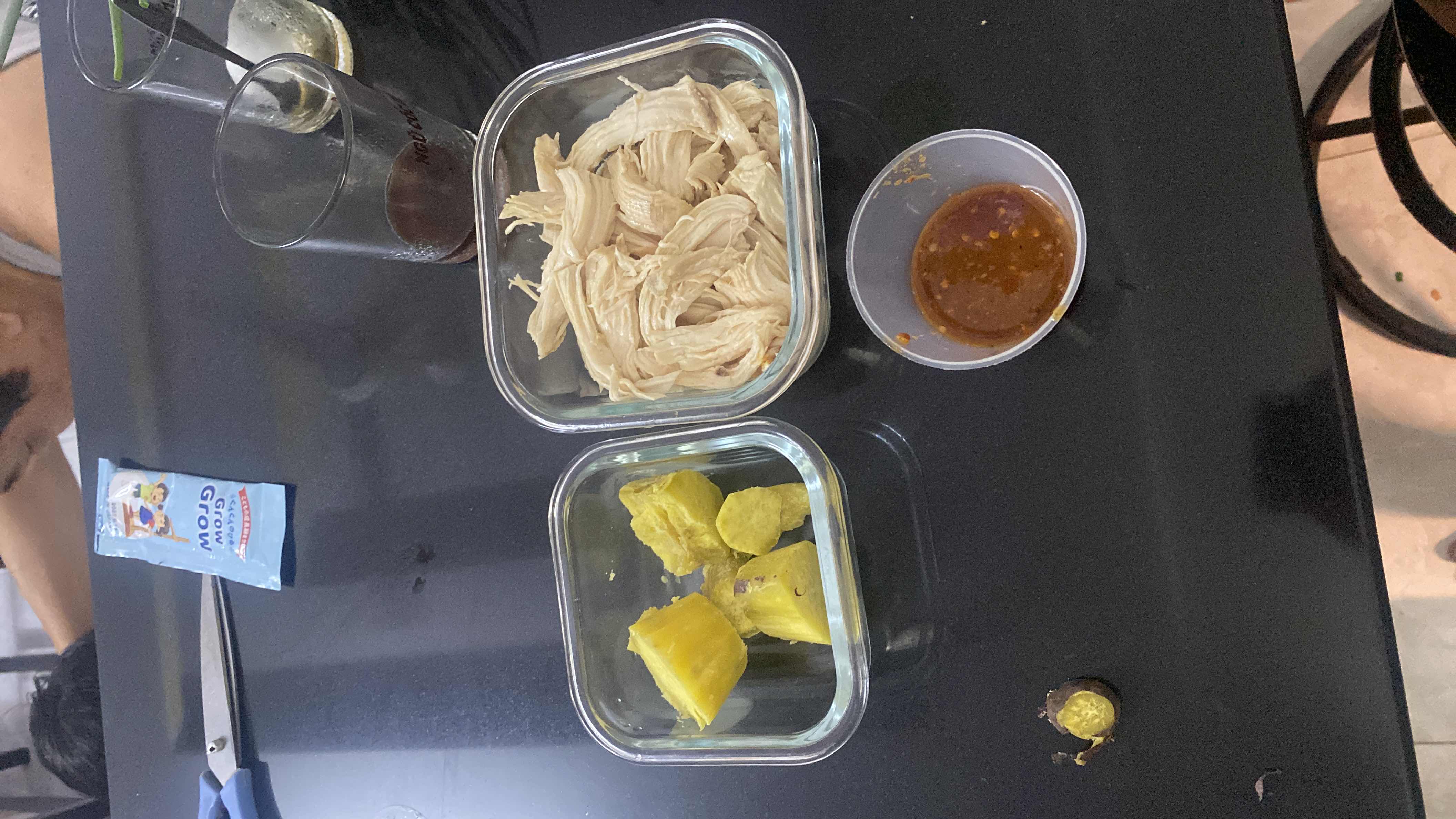A meal consisting of shredded chicken breast, sweet potato chunks, and a small portion of dipping sauce, providing a balanced mix of protein, carbs, and fats.