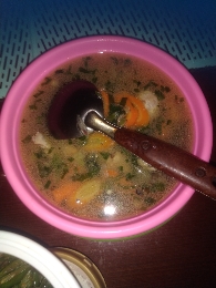 A light chicken soup with vegetables, including carrots and herbs, served in a pink bowl.