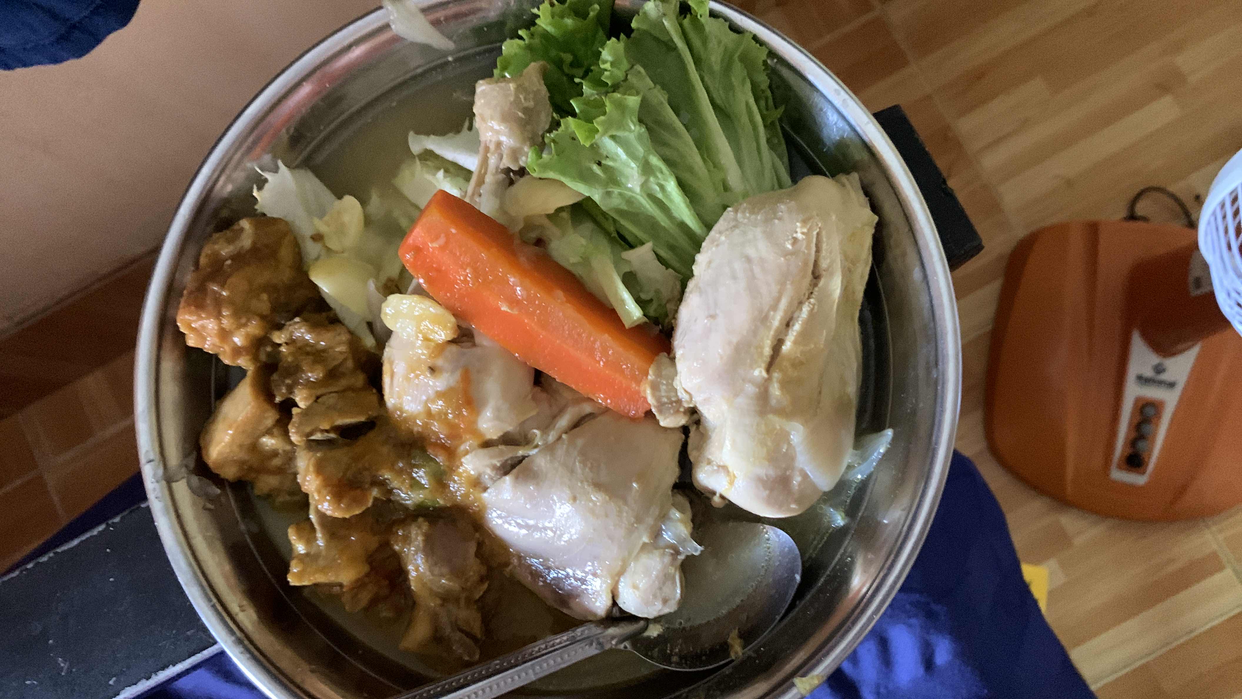 A nutritious meal consisting of boiled chicken, vegetables (carrot, lettuce, cabbage), and broth, providing a balanced mix of protein, carbs, and fats.