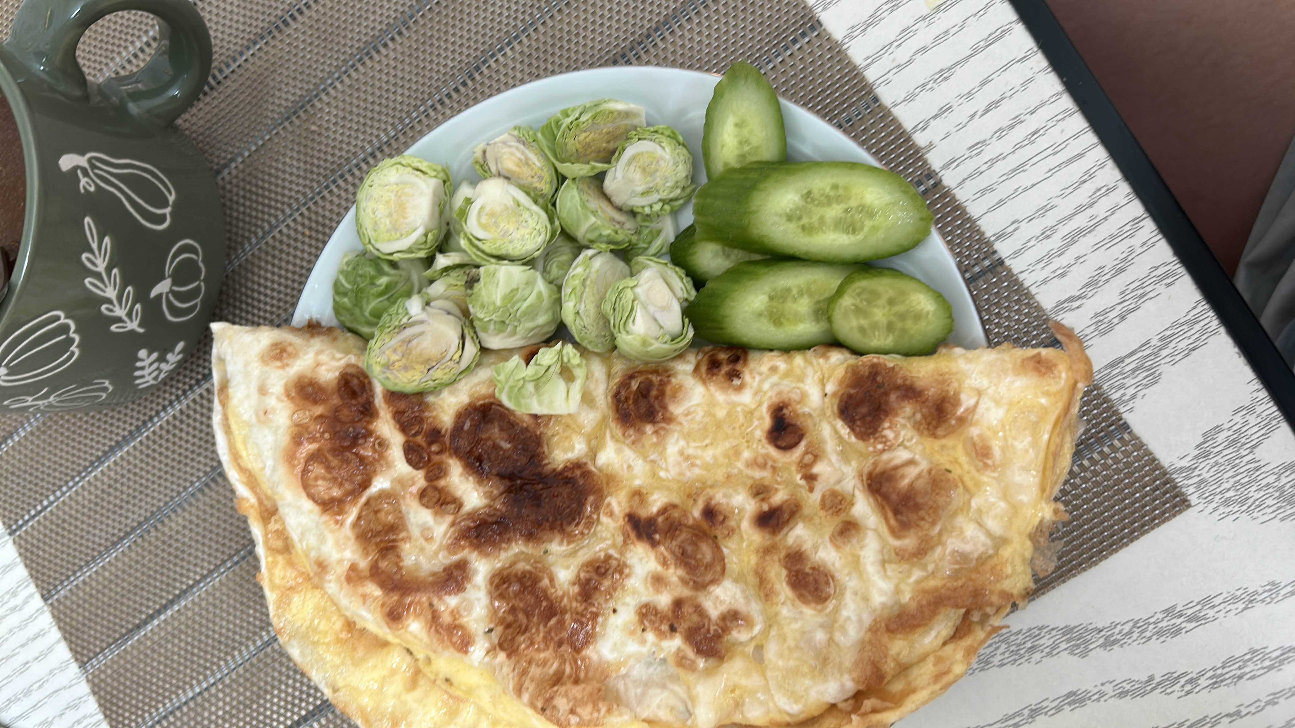 A balanced meal consisting of an omelette, fresh Brussels sprouts, and cucumber slices, providing a good mix of protein, fats, and fiber.