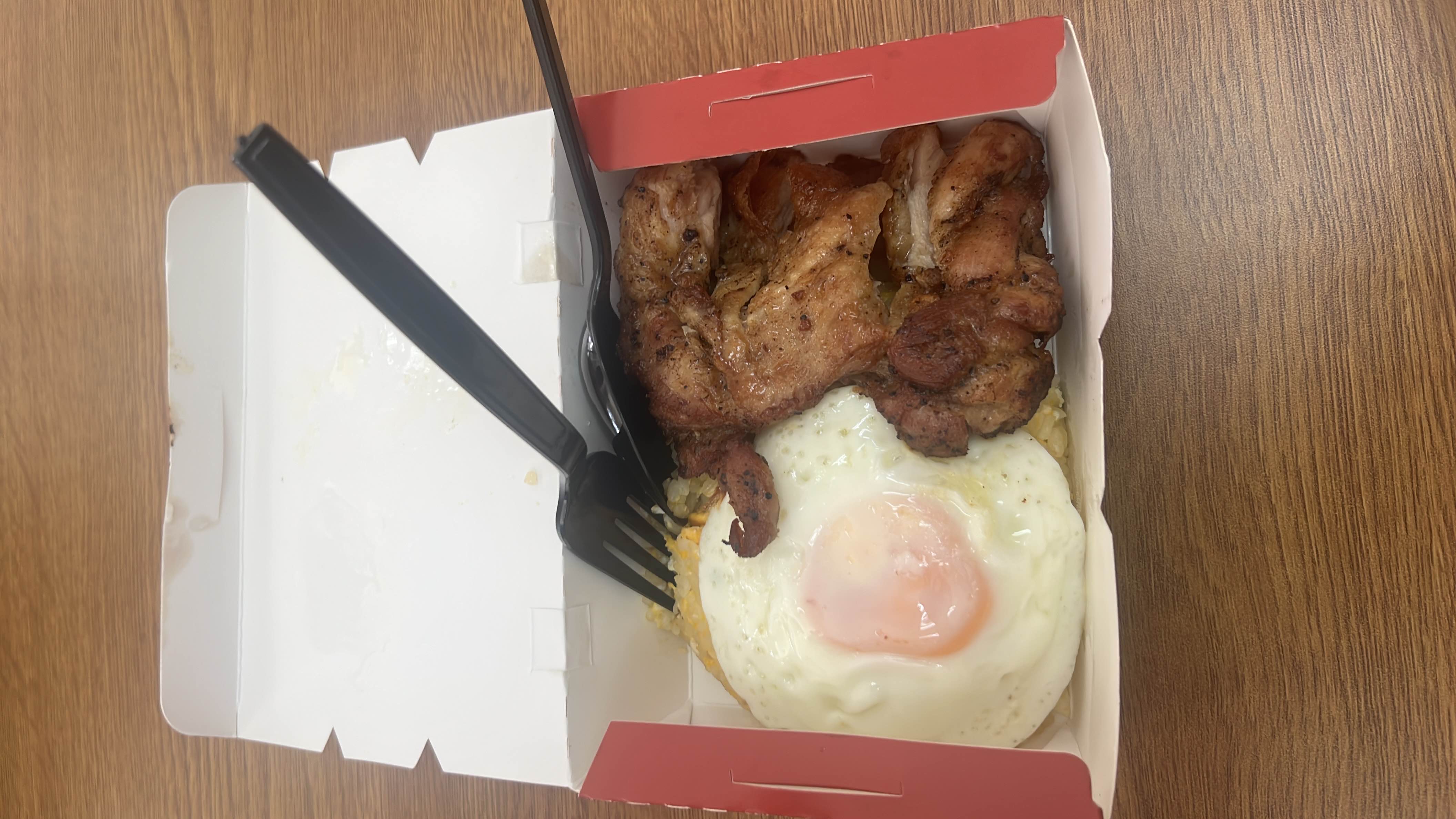 A serving of egg fried rice topped with a sunny side up egg and a chicken chop, providing a balanced mix of carbohydrates, protein, and fats.