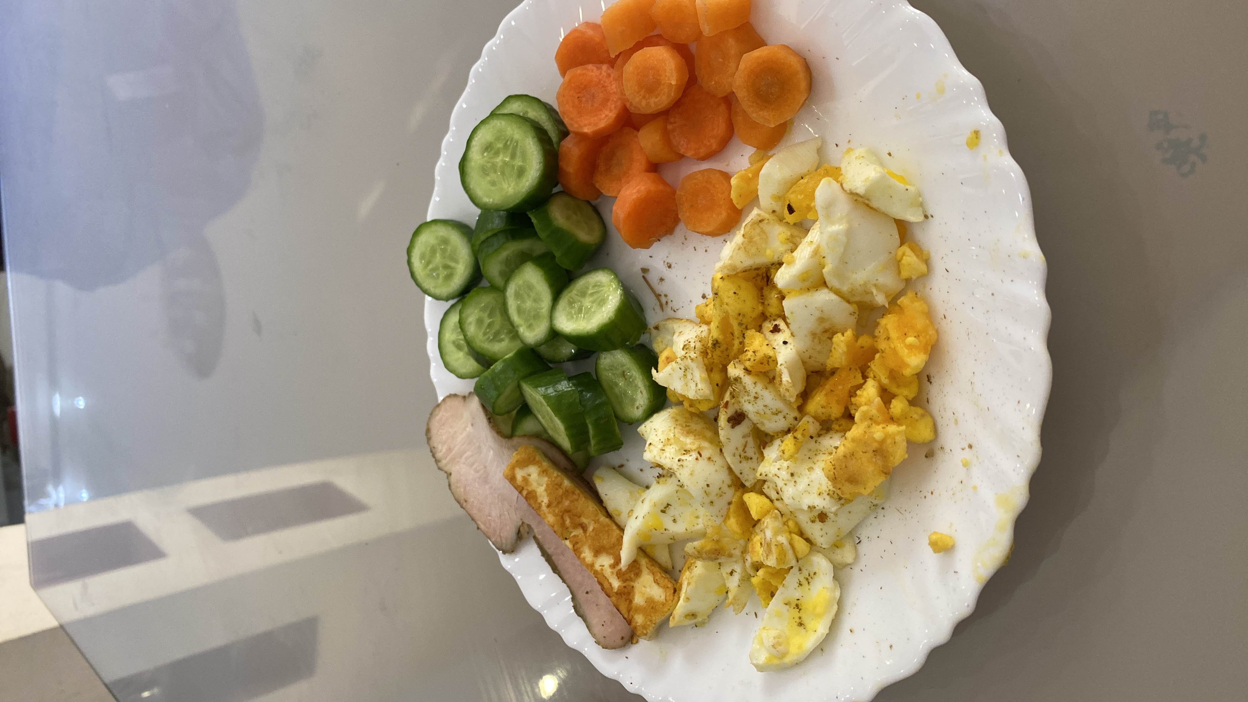 A healthy plate consisting of boiled eggs, cucumber slices, carrots, grilled paneer, and sliced chicken, providing a balanced mix of protein, fats, and carbs.