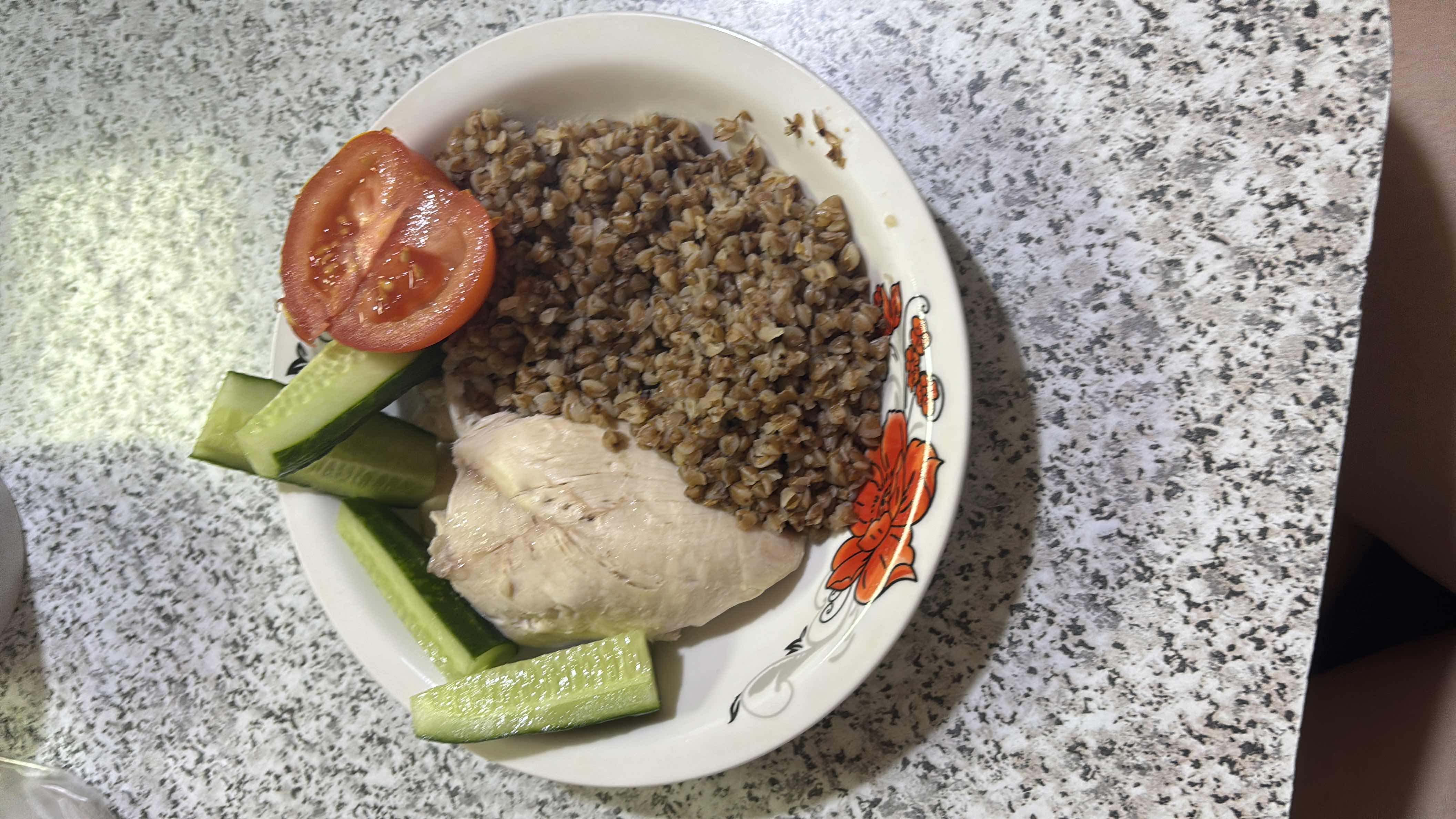A healthy meal consisting of boiled chicken breast, buckwheat, fresh cucumber, and tomato slices.
