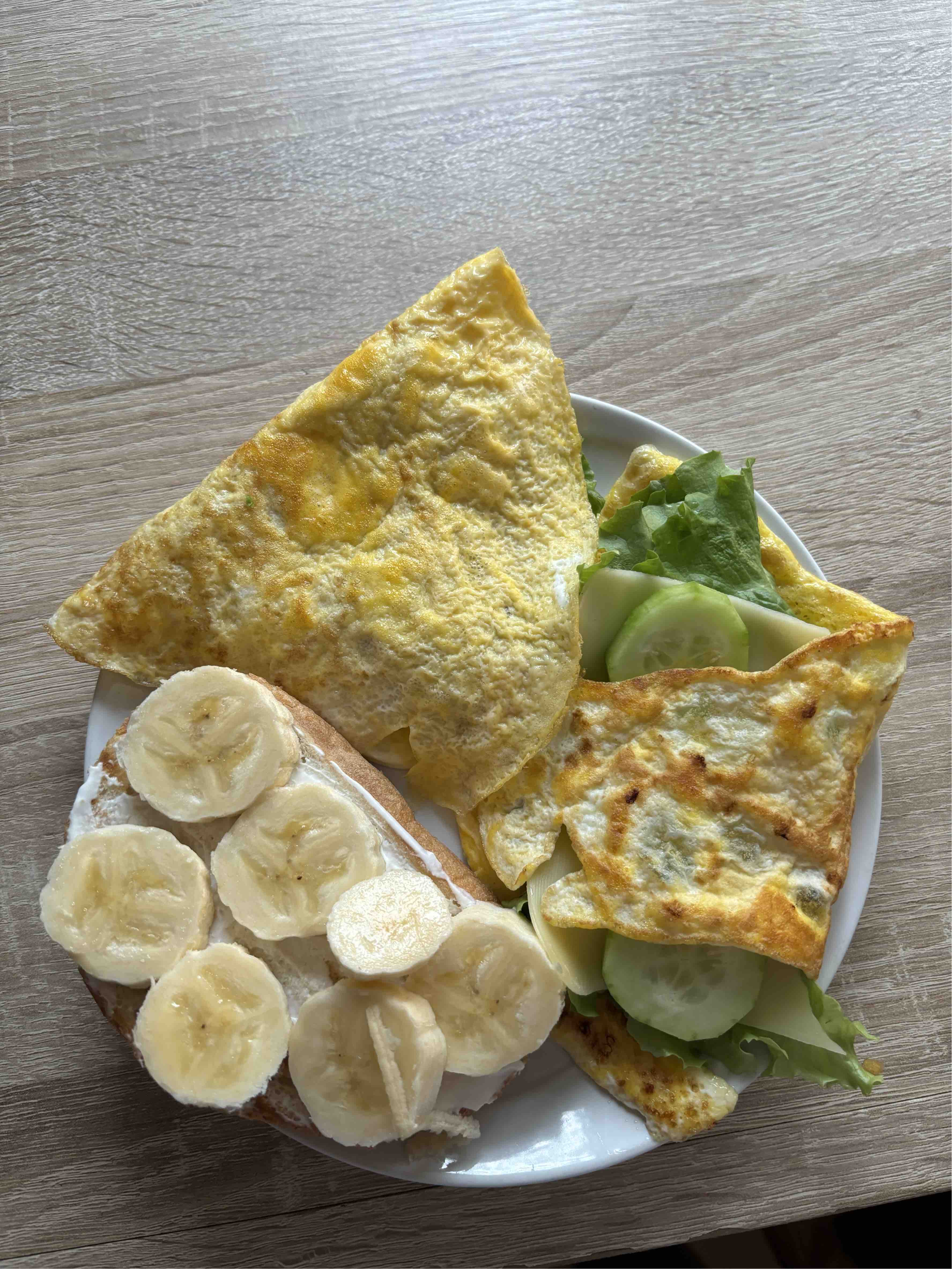 A balanced meal consisting of an egg omelette, bread topped with banana slices, and a side of lettuce and cucumber.