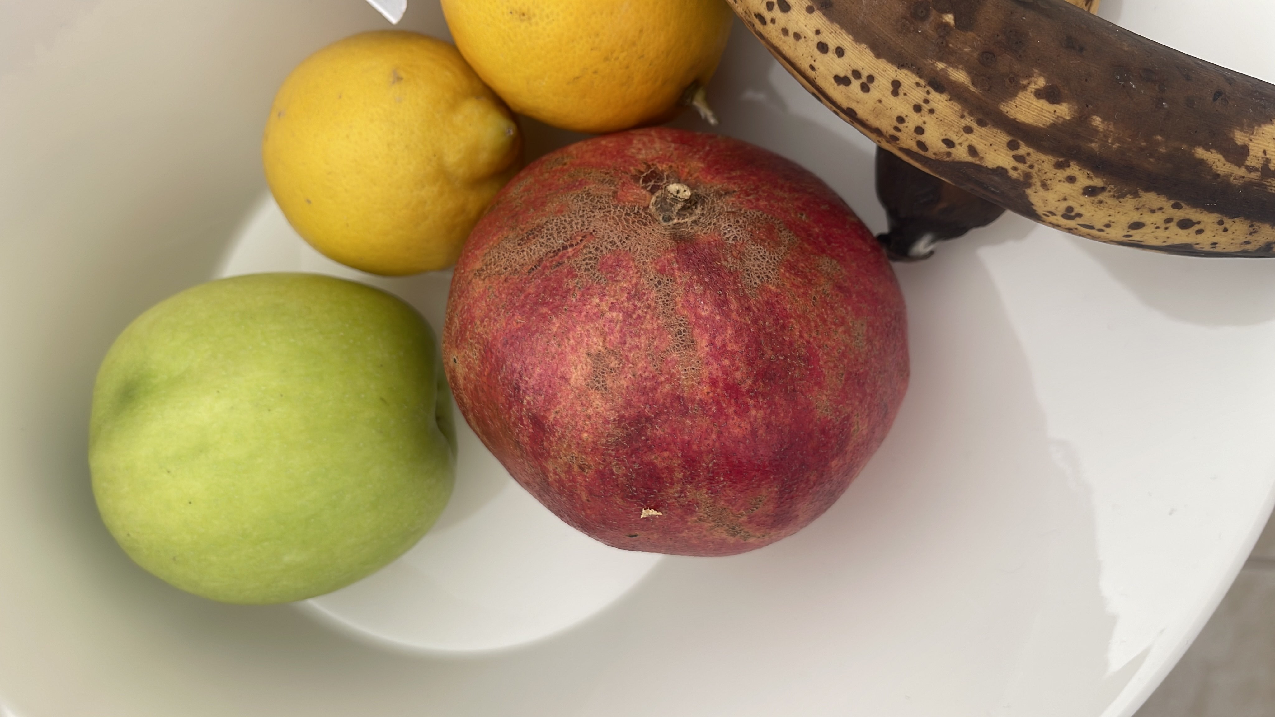 A bowl containing a green apple, a pomegranate, a ripe banana, and two lemons, providing a mix of vitamins, fiber, and natural sugars.