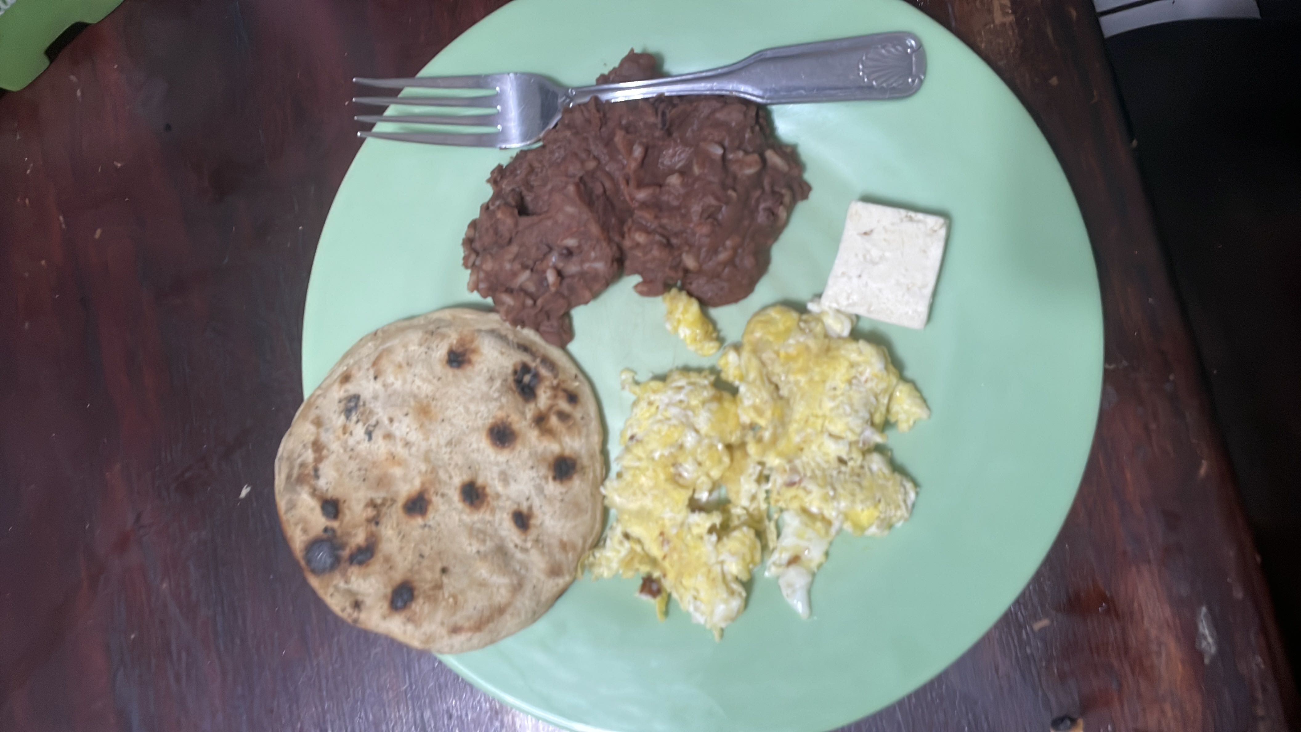 A balanced meal consisting of a tortilla, scrambled eggs, refried beans, and a small piece of tofu, providing a mix of protein, carbs, and fats.