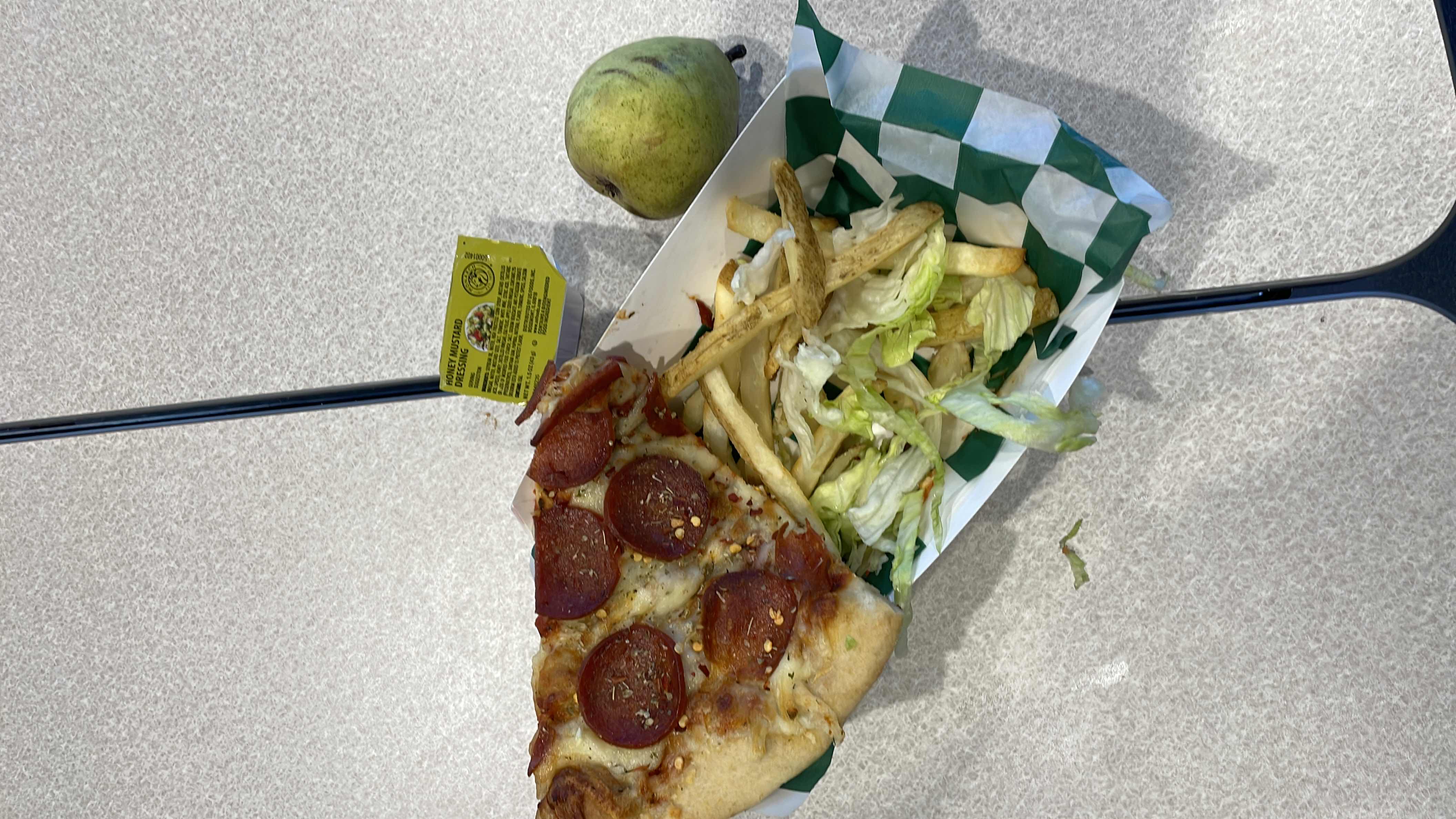 A meal consisting of a pepperoni pizza slice, french fries, lettuce salad with honey mustard dressing, and a pear.
