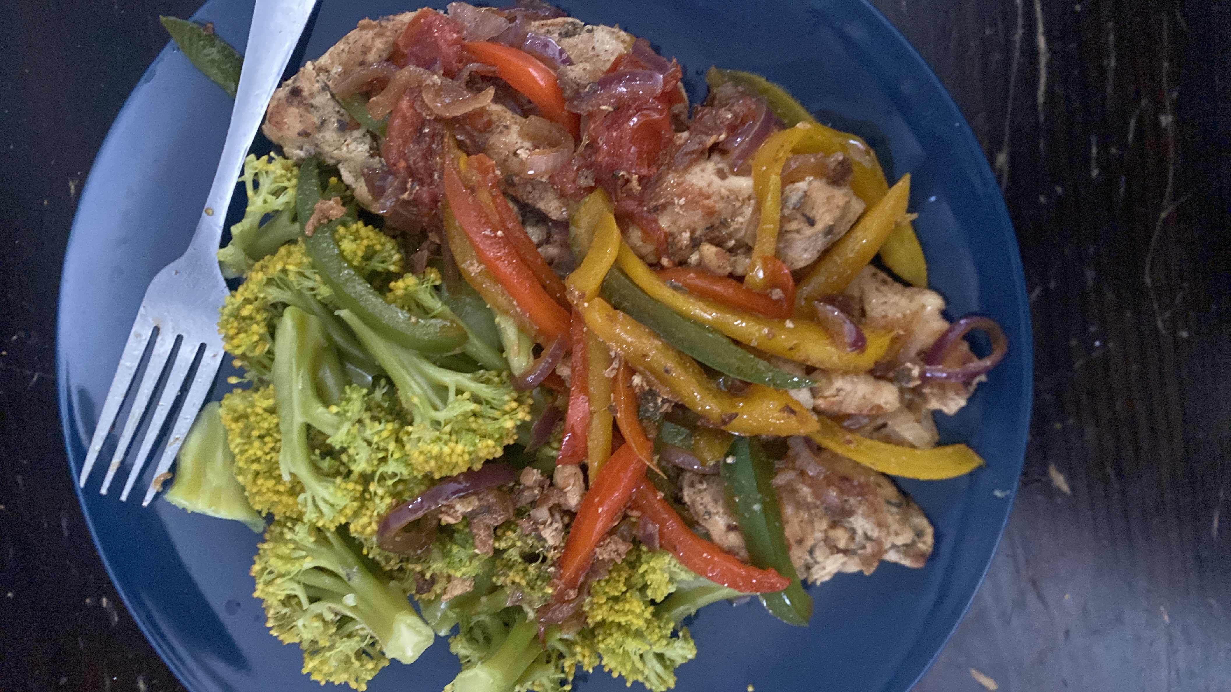A healthy dish consisting of steamed broccoli, sautéed chicken, and a mix of bell peppers, onions, and tomatoes.