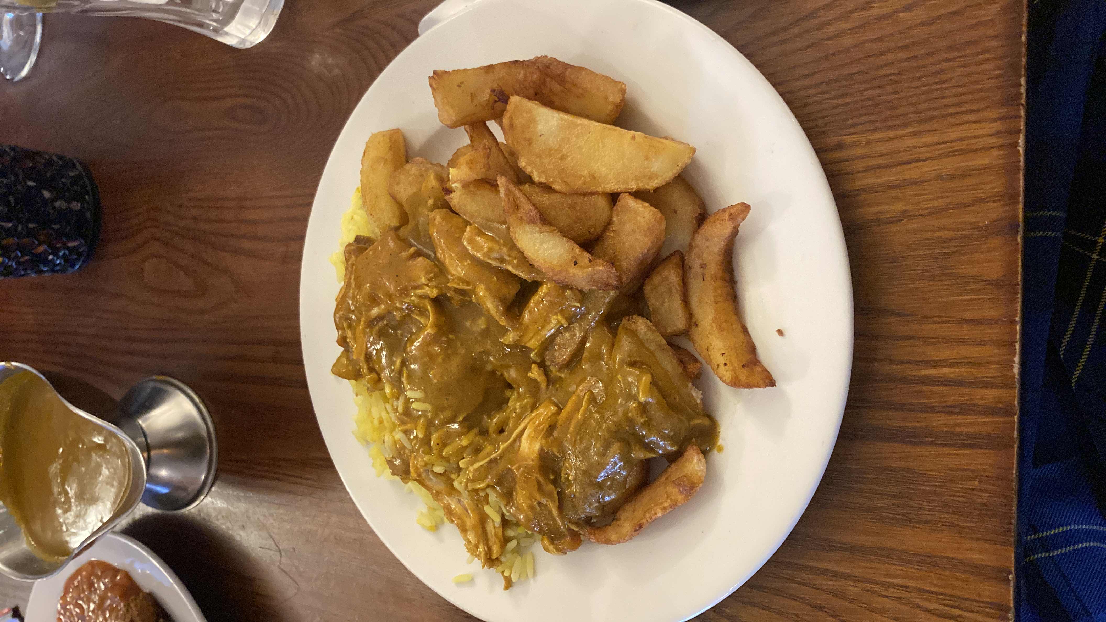 A plate of chicken curry served with potato wedges and rice, providing a balanced mix of protein, carbs, and fats.