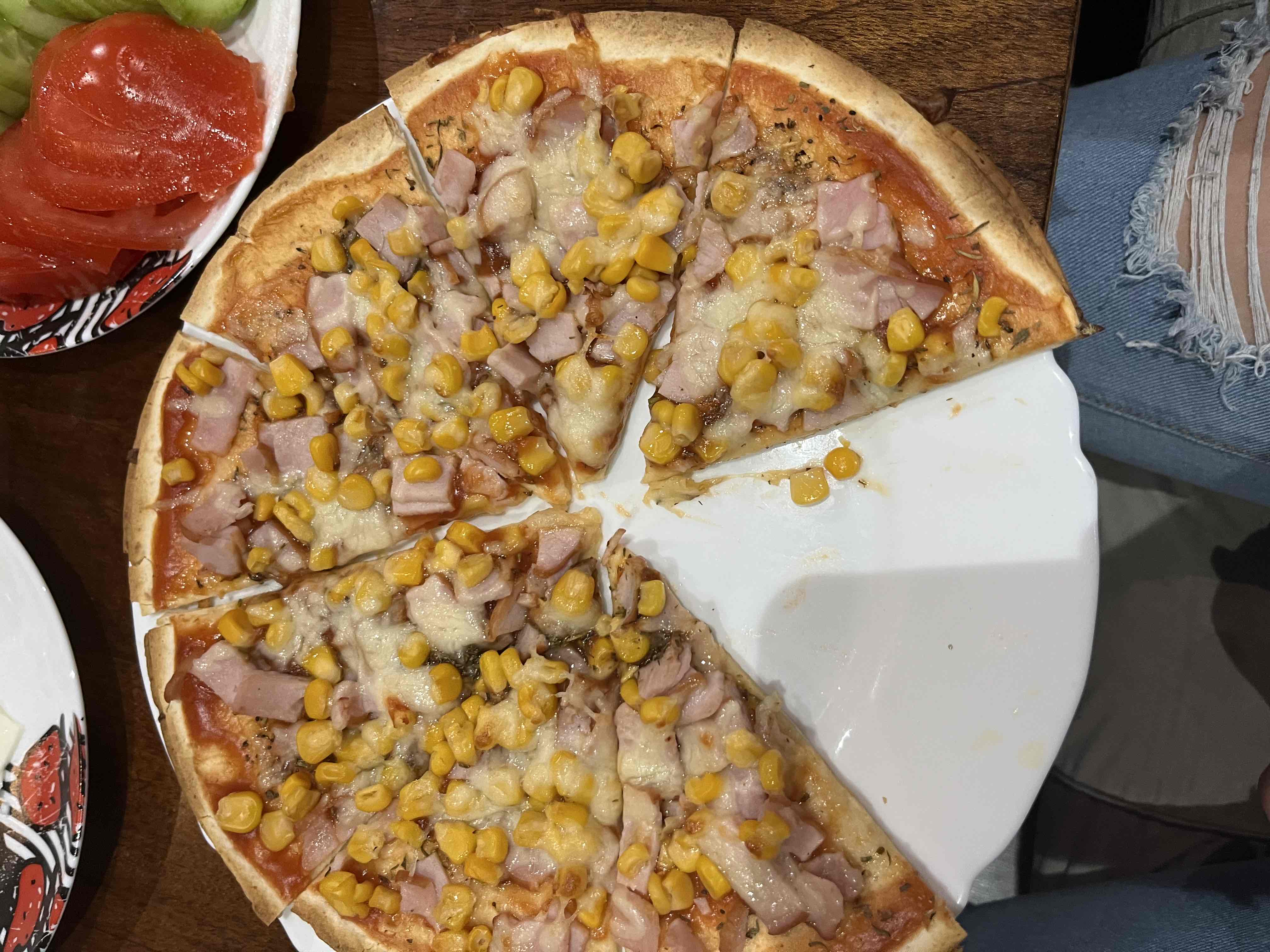 A pizza topped with cheese, ham, and corn, served on a thin crust.