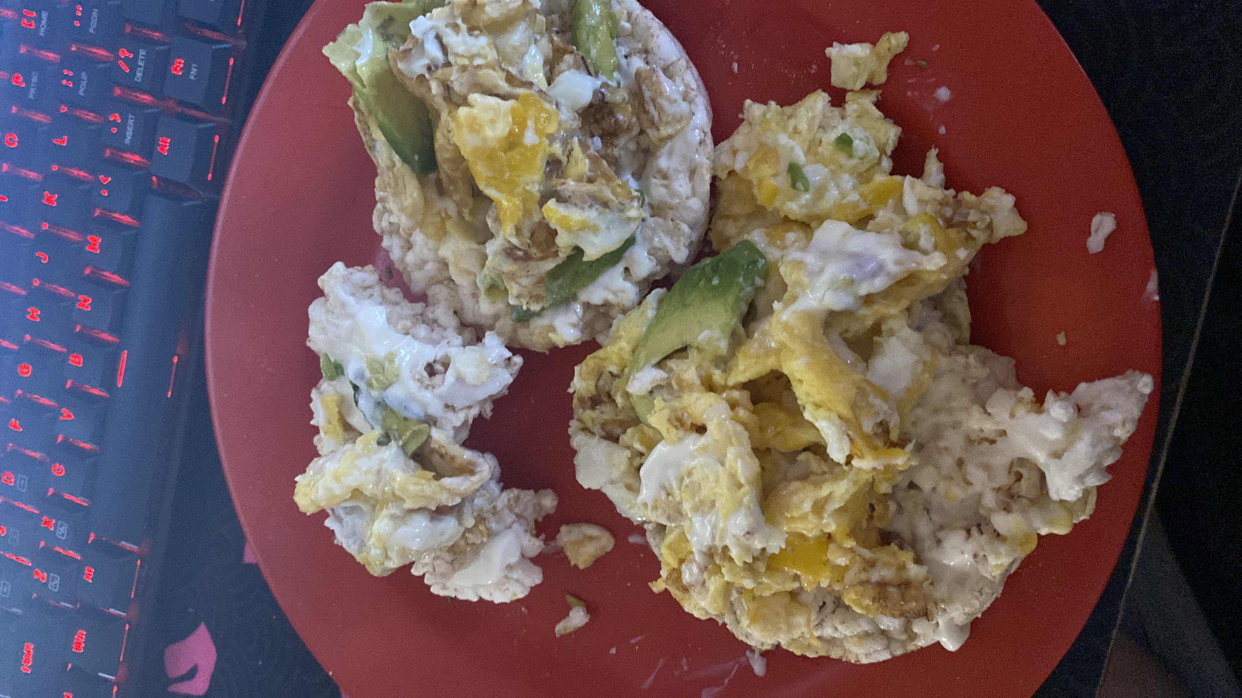A dish consisting of scrambled eggs, avocado slices, cheese, and rice cakes, providing a balanced mix of protein, carbs, and fats.