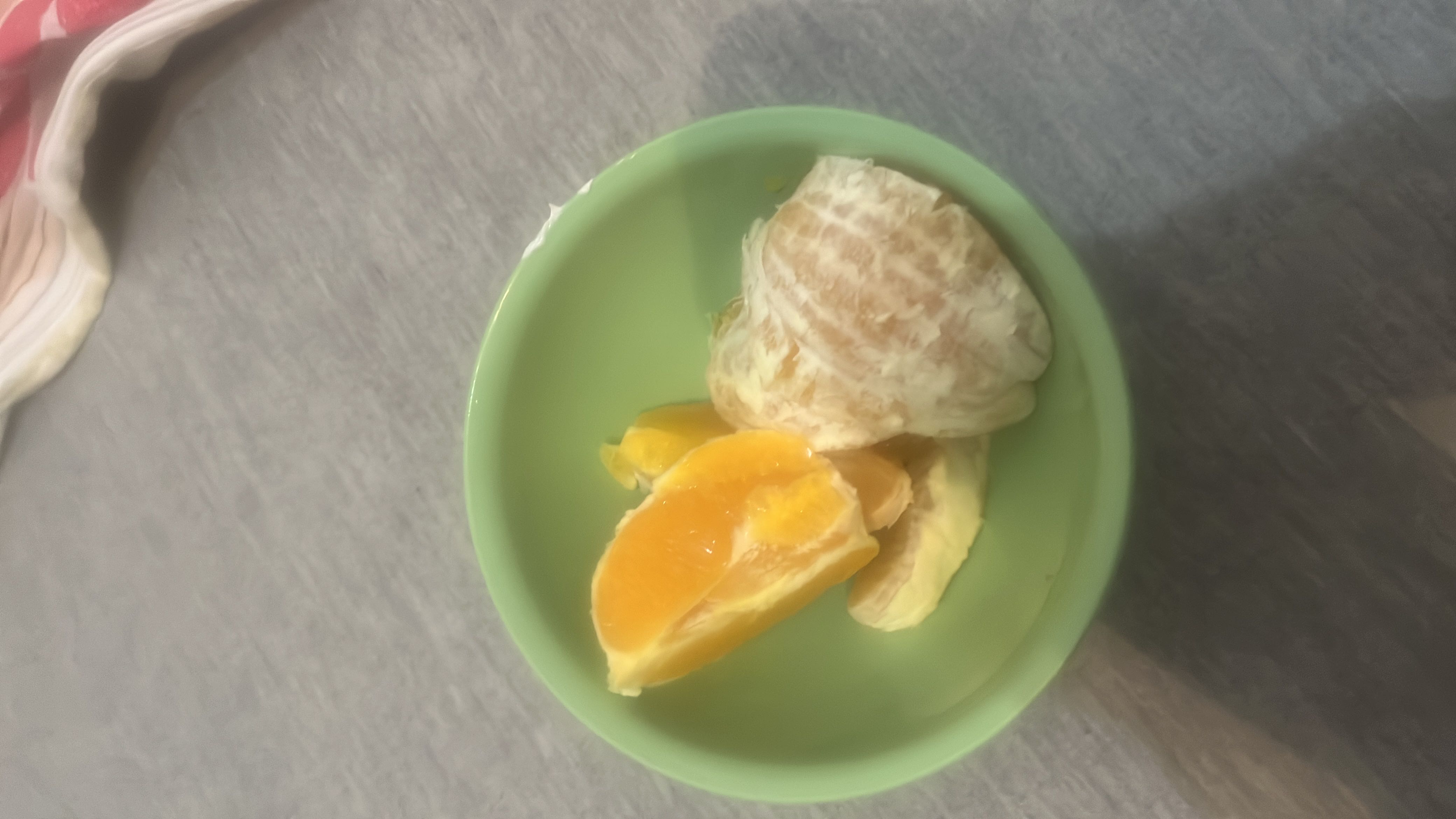 The image shows a peeled orange and orange slices in a green bowl, providing a healthy and low-calorie snack rich in vitamin C.