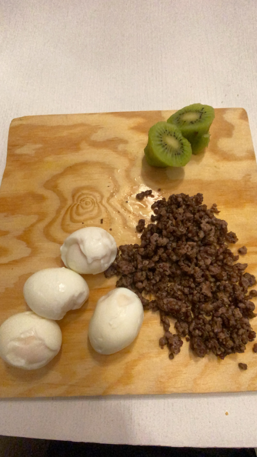 A meal consisting of boiled eggs, ground beef, and sliced kiwi, providing a balanced mix of protein, fats, and carbohydrates.