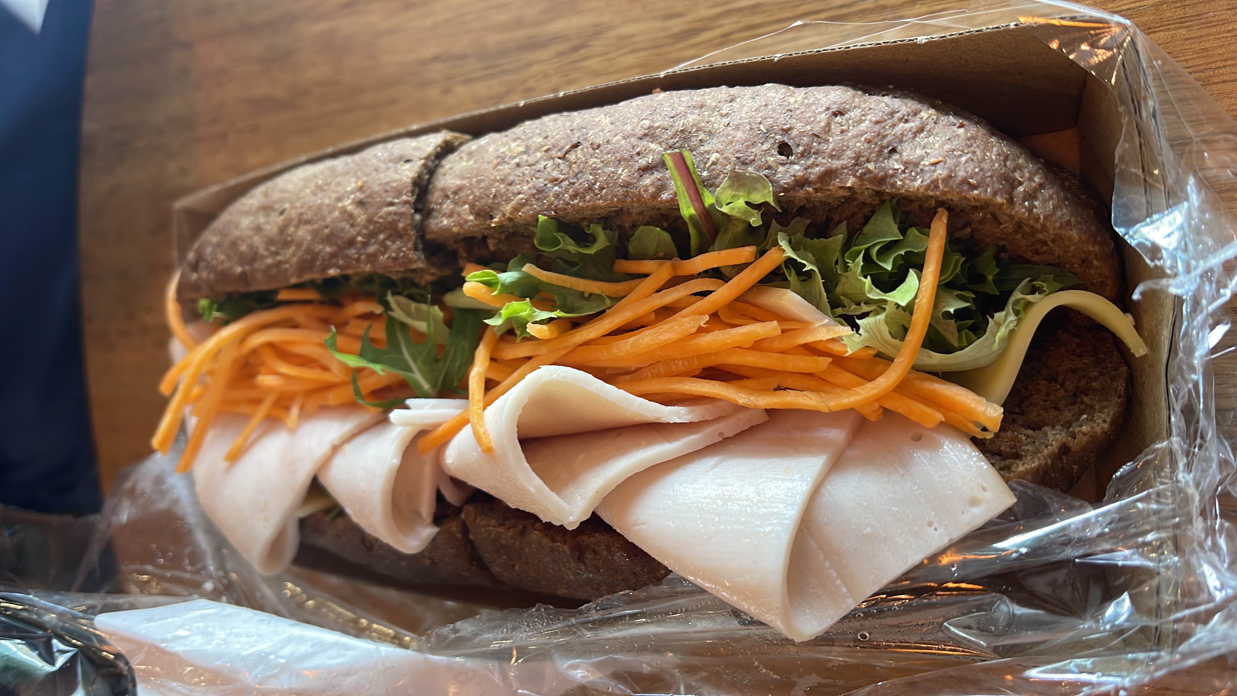A healthy sandwich made with whole grain bread, turkey slices, fresh lettuce, carrot strips, and a slice of cheese.