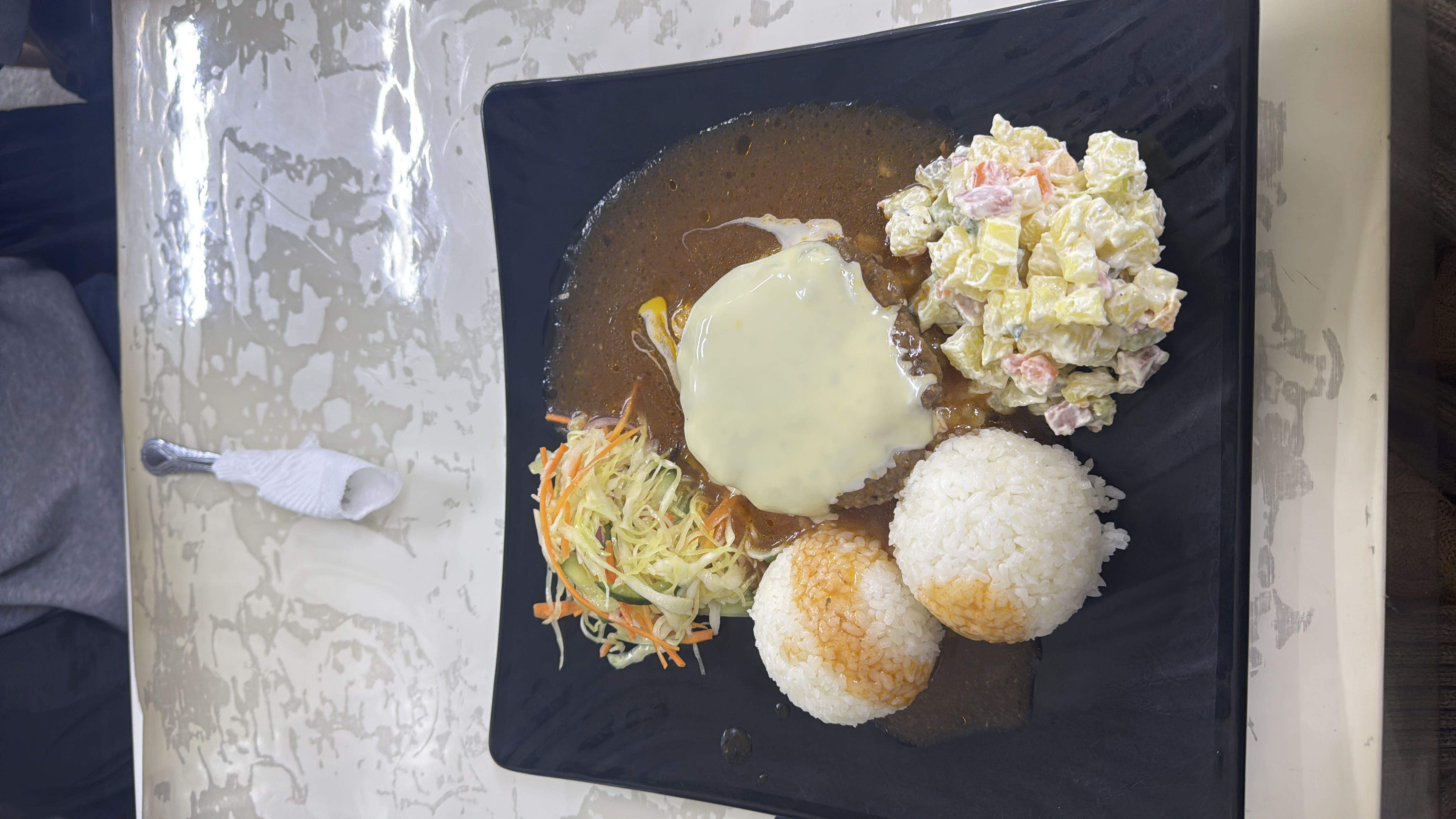 A balanced meal consisting of rice, a beef patty topped with cheese, vegetable salad, and potato salad, served with a savory sauce.