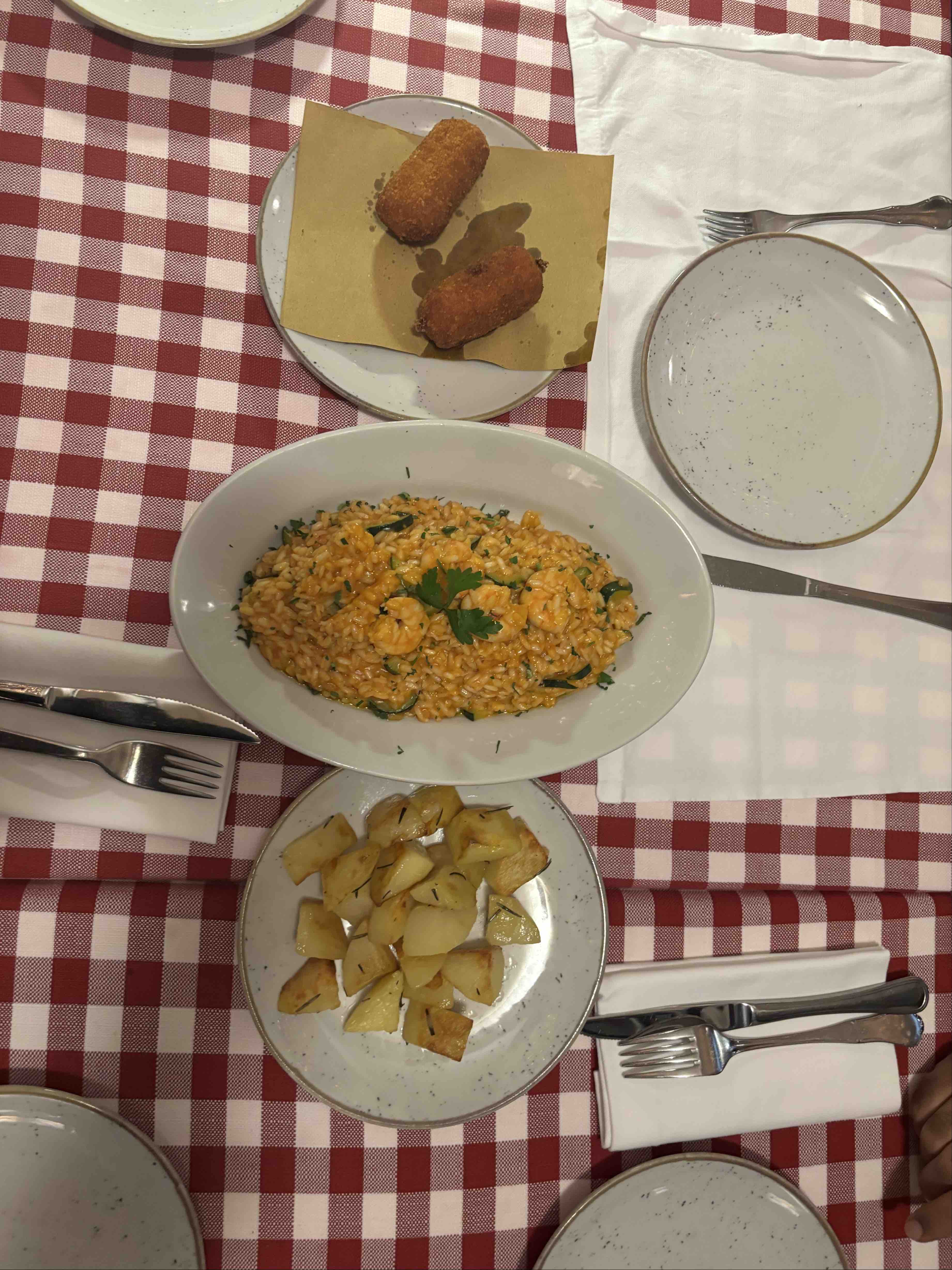 The image shows a meal consisting of risotto, roasted potatoes, and croquettes, served on a checkered tablecloth.