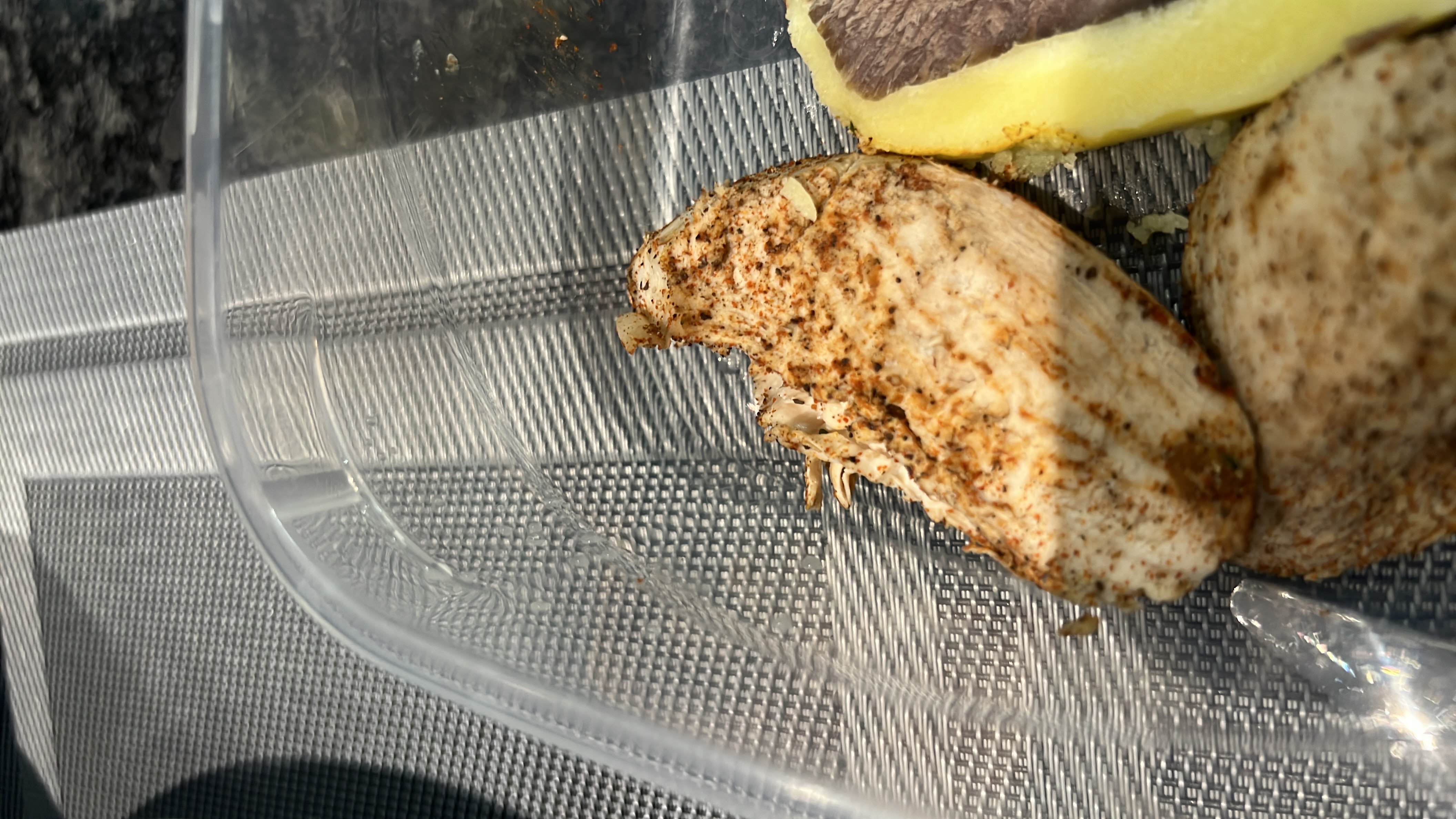 A meal consisting of grilled chicken breast and a potato wedge, seasoned with spices.