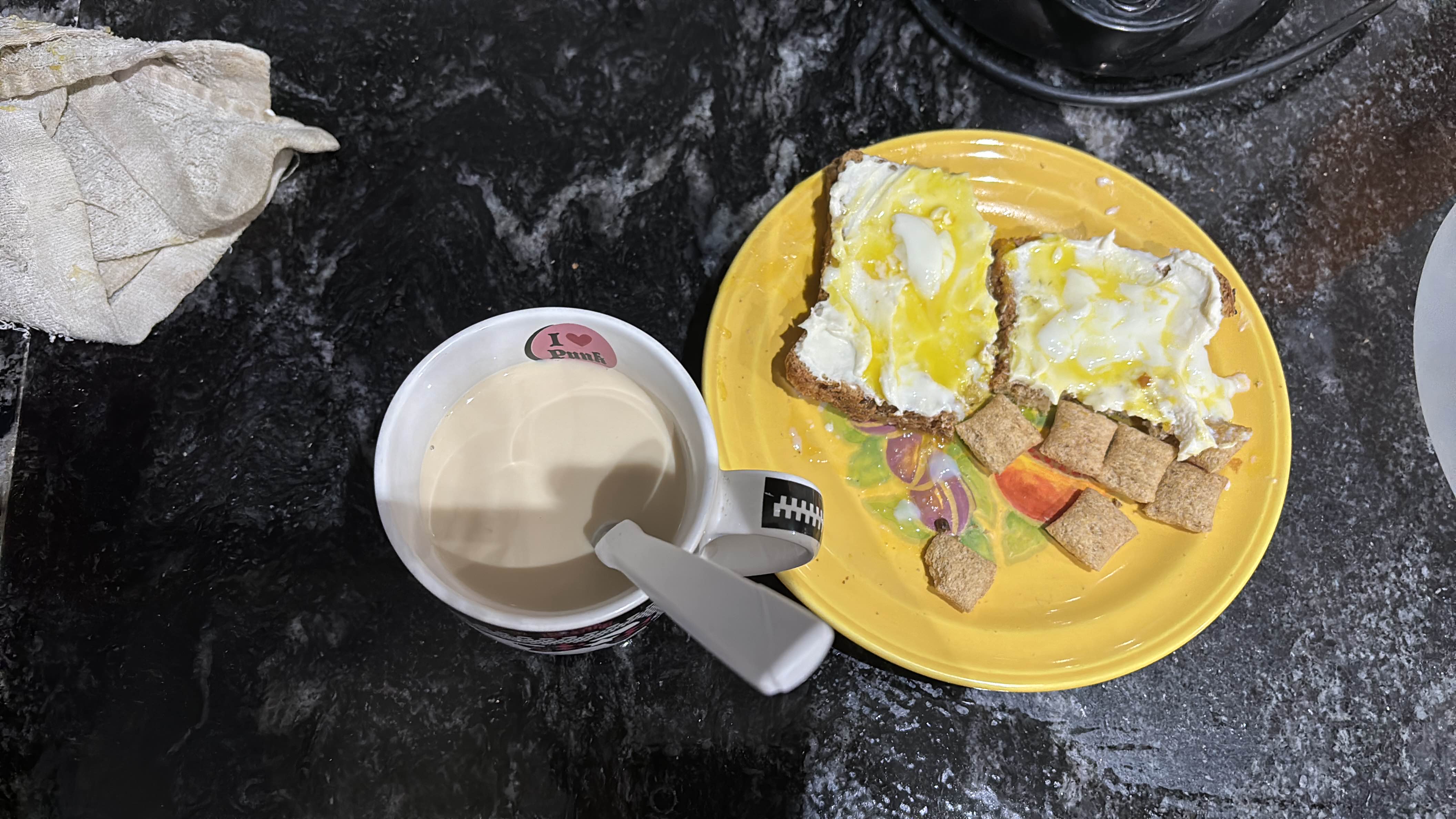 A breakfast meal consisting of bread with egg, cereal cubes, and a cup of milk tea.