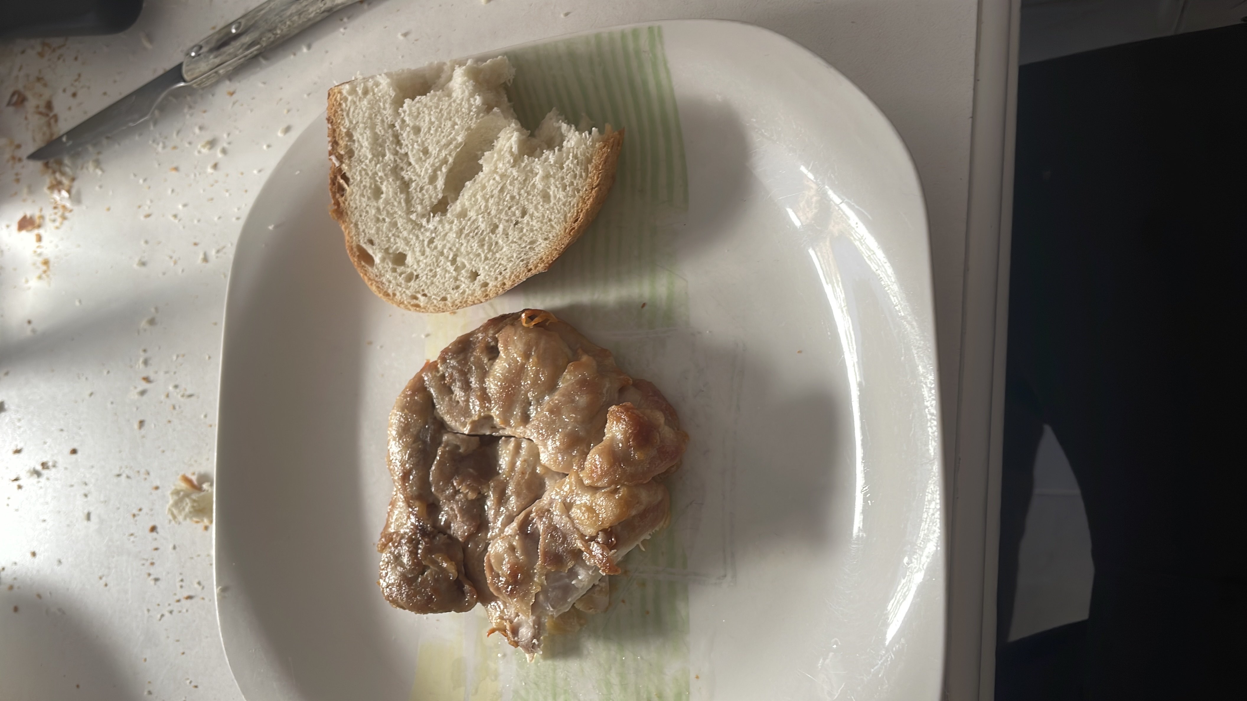 A plate containing a piece of grilled meat and a slice of bread, providing a balanced mix of protein, carbs, and fats.