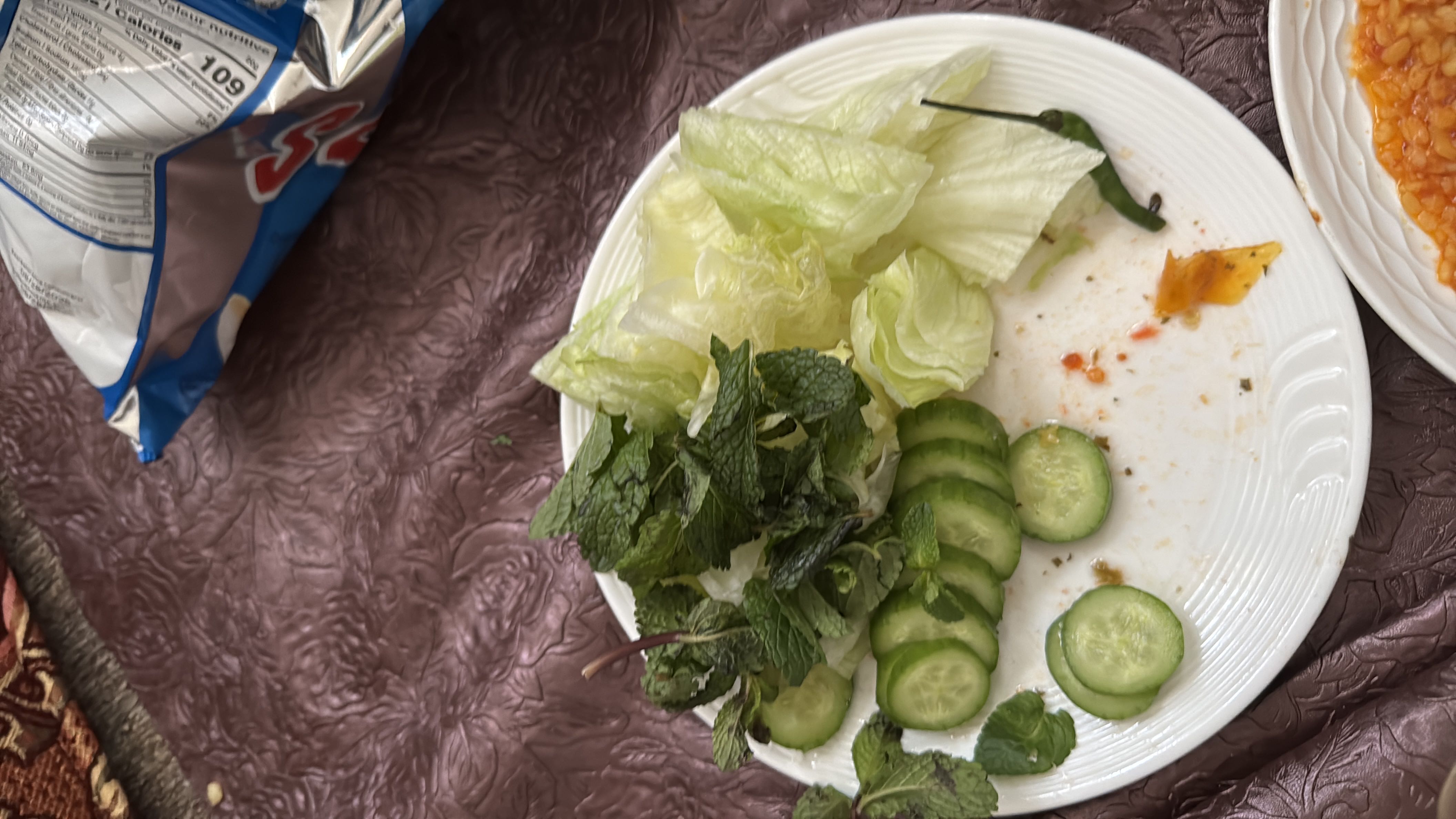 A plate of fresh vegetables including cucumber slices, lettuce, mint leaves, and a green chili, providing a low-calorie and nutrient-rich option.