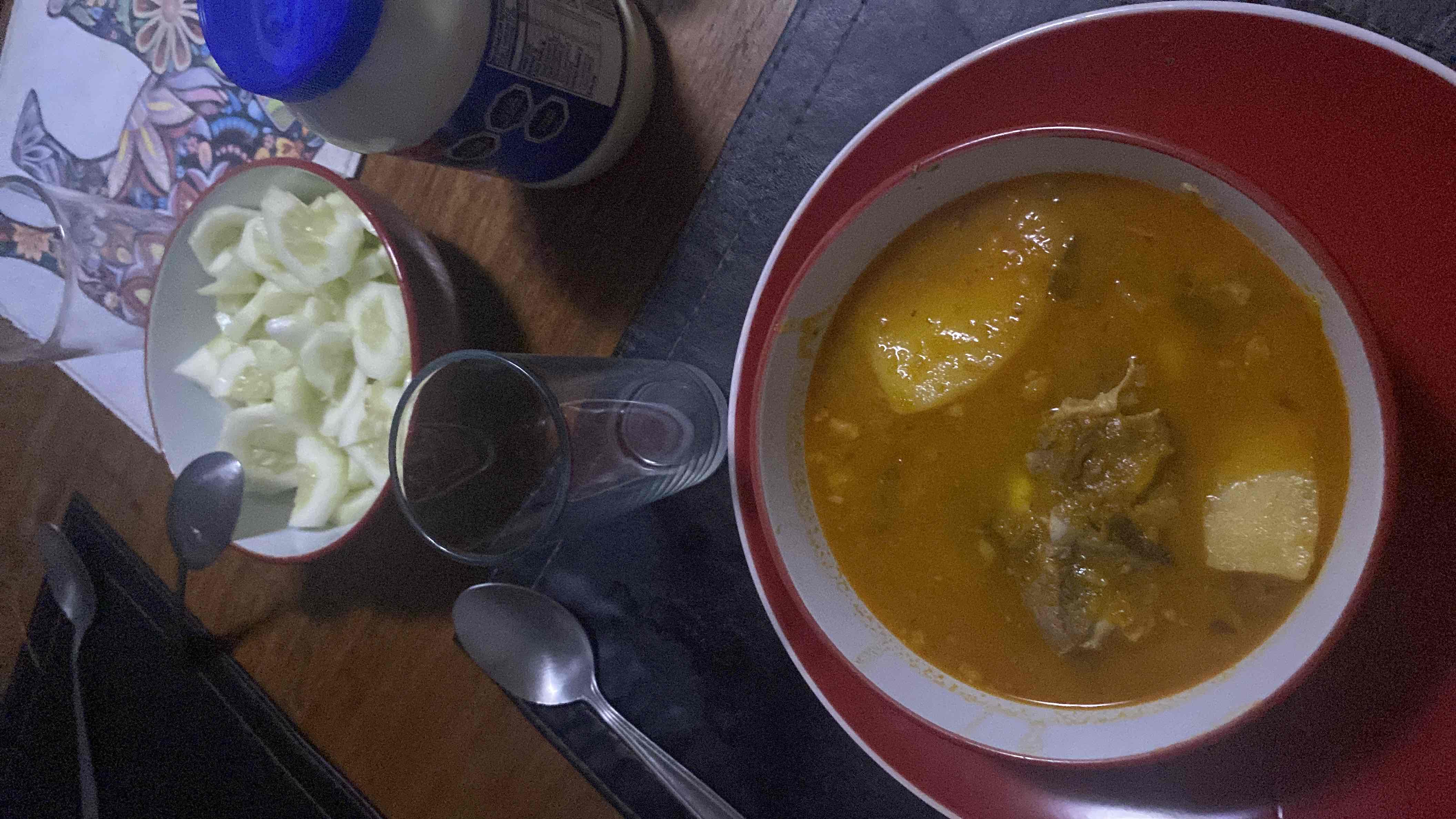 A hearty soup with potatoes, meat, and a side of fresh cucumber slices, providing a balanced mix of protein, carbs, and fats.