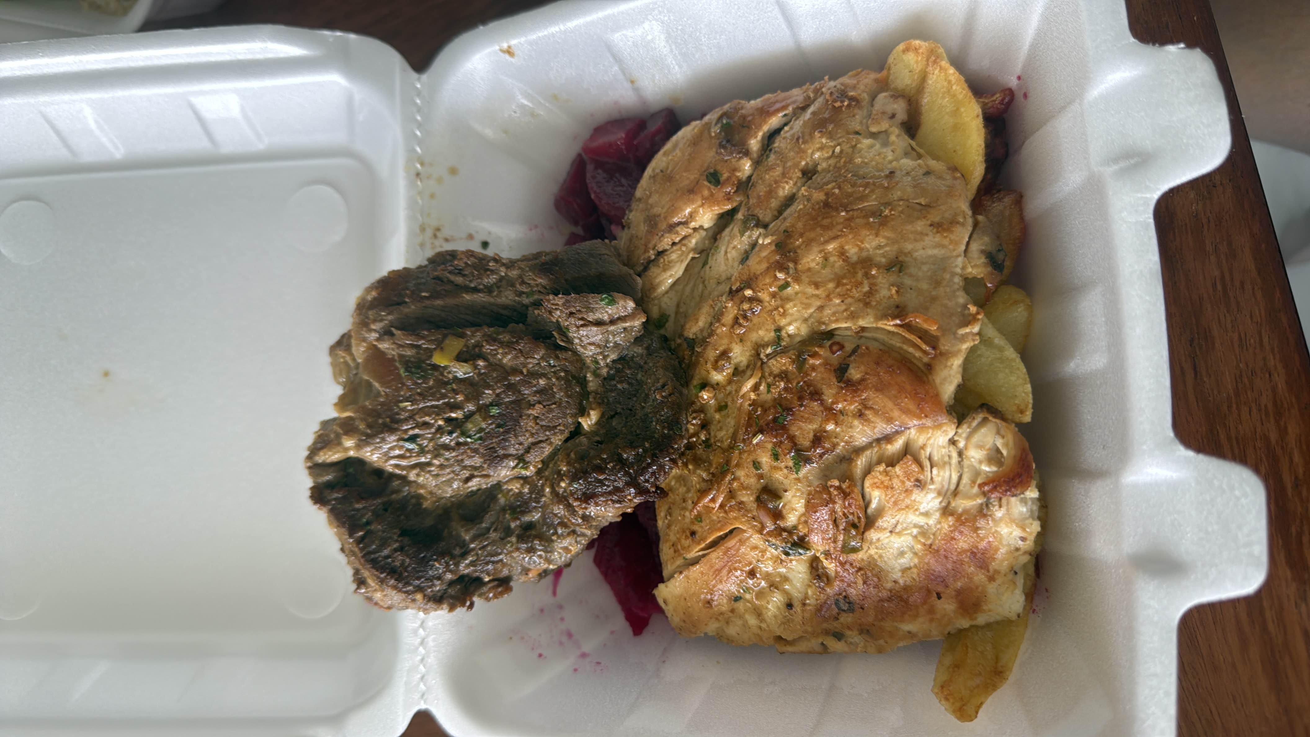A meal consisting of grilled chicken, beef steak, and potato wedges, served in a takeout container.