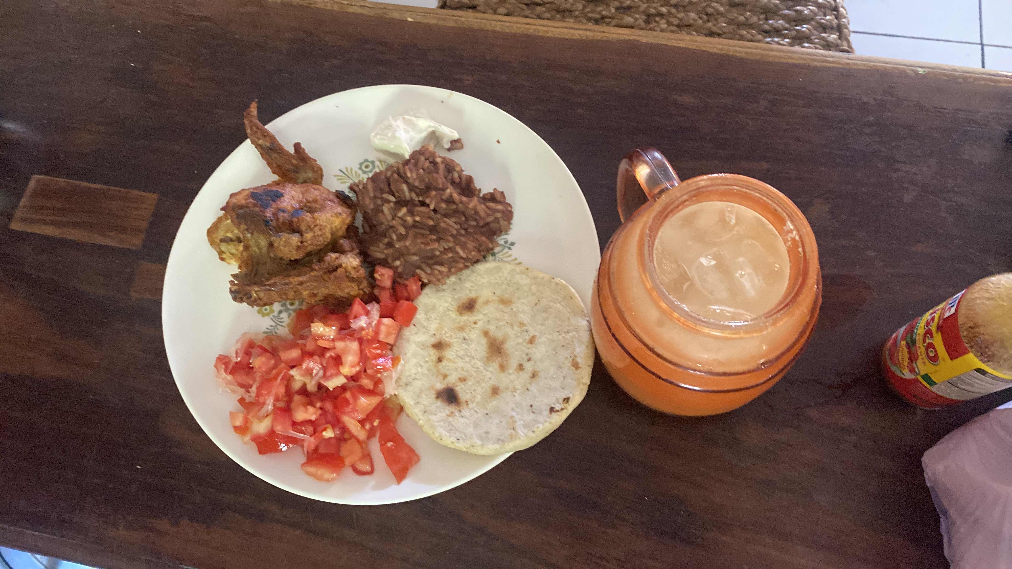 A balanced meal consisting of grilled chicken, tomato salad, refried beans, a corn tortilla, and a glass of orange juice.