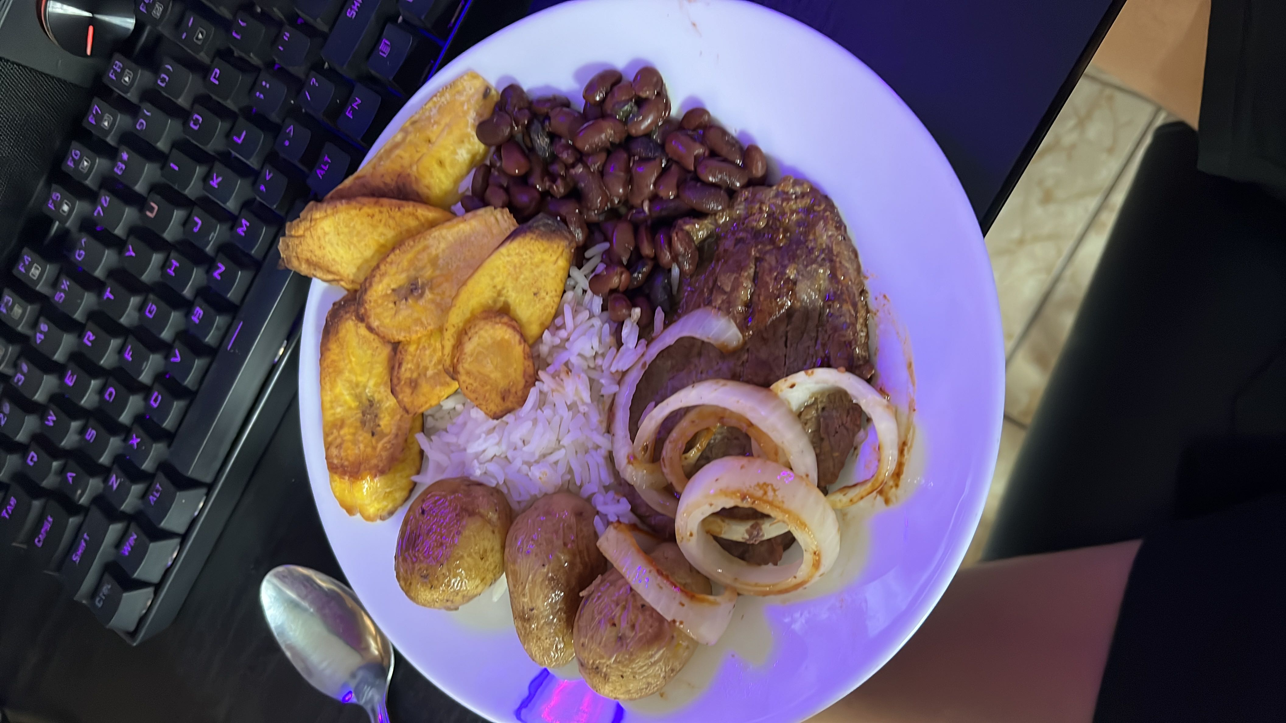 A balanced meal consisting of rice, fried plantains, beans, beef, and potatoes, providing a mix of protein, carbohydrates, and fats.