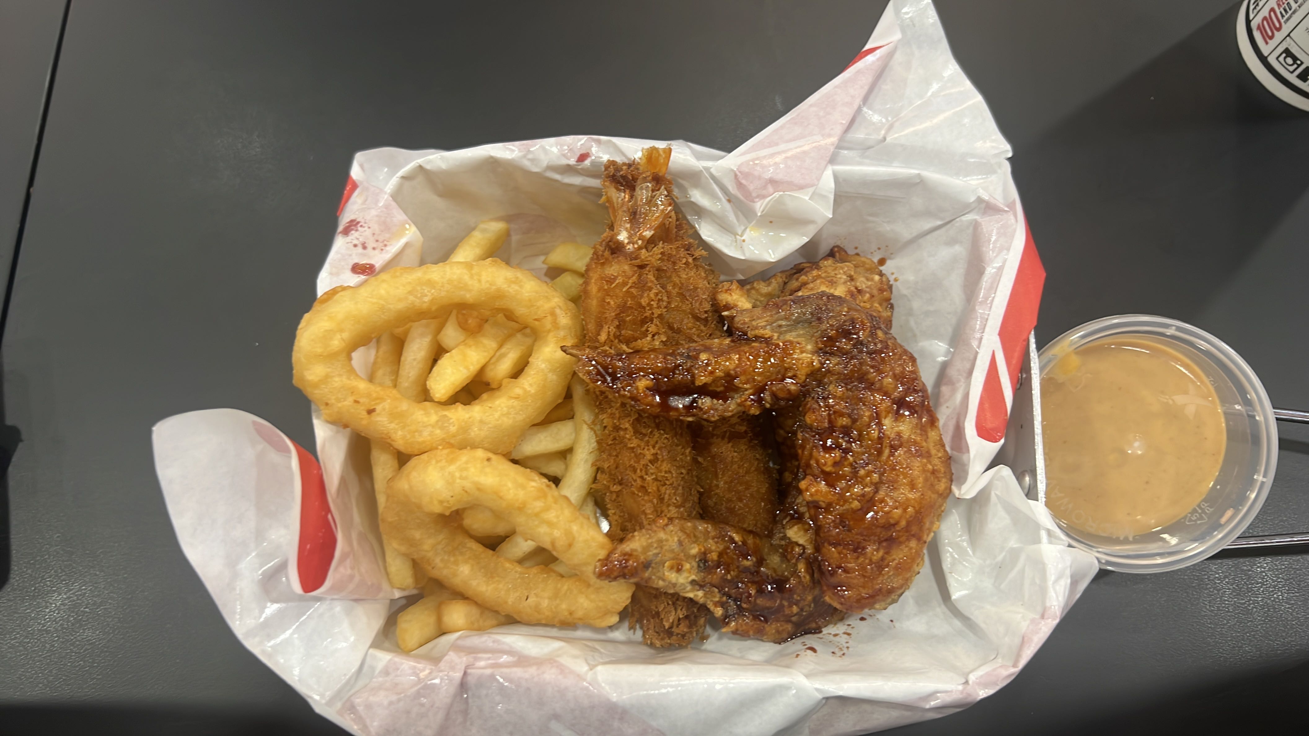 A meal consisting of fried chicken, onion rings, french fries, and fried shrimp, served with a dipping sauce.
