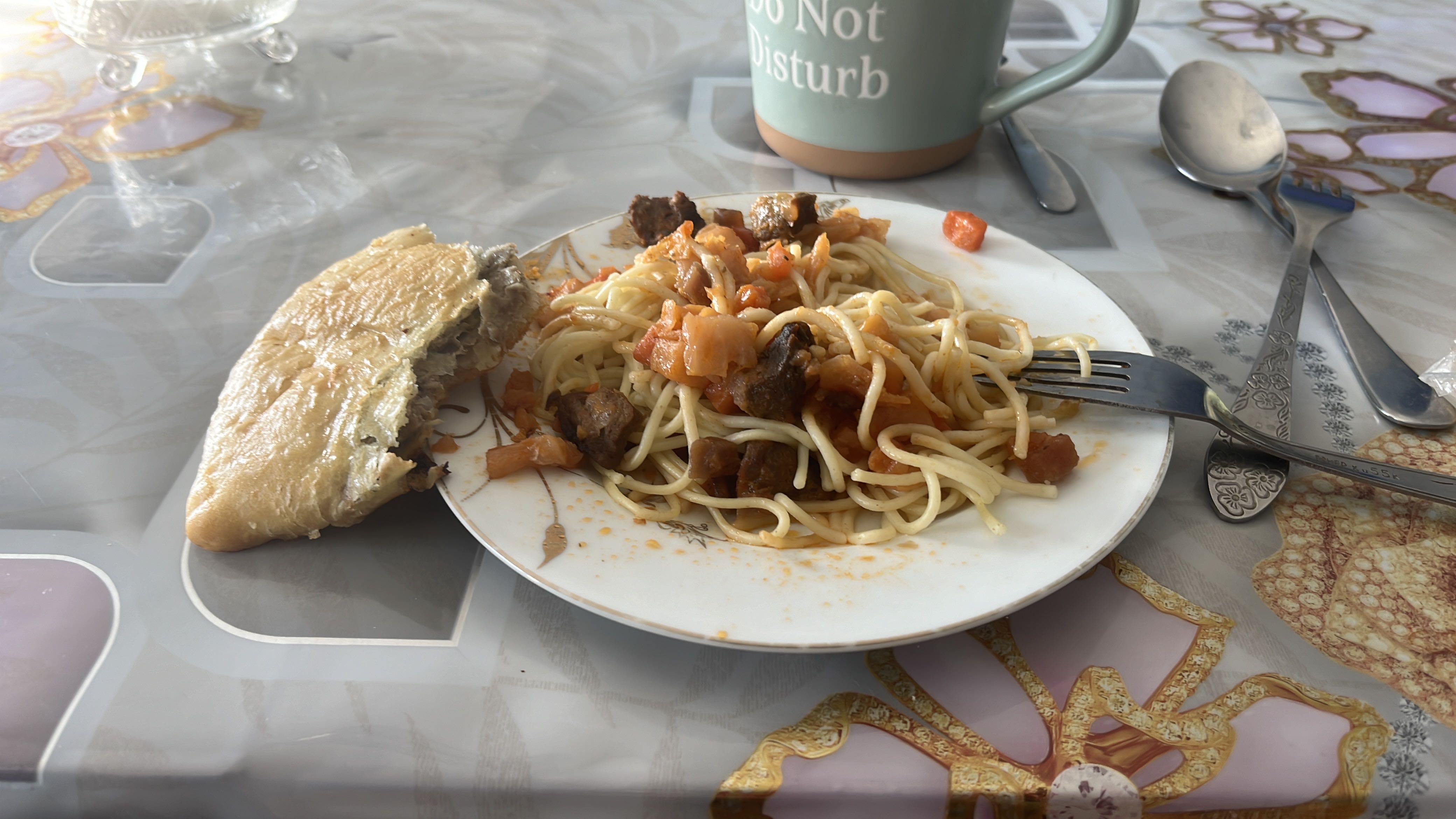 A plate of spaghetti with beef and tomato sauce, accompanied by a piece of bread.