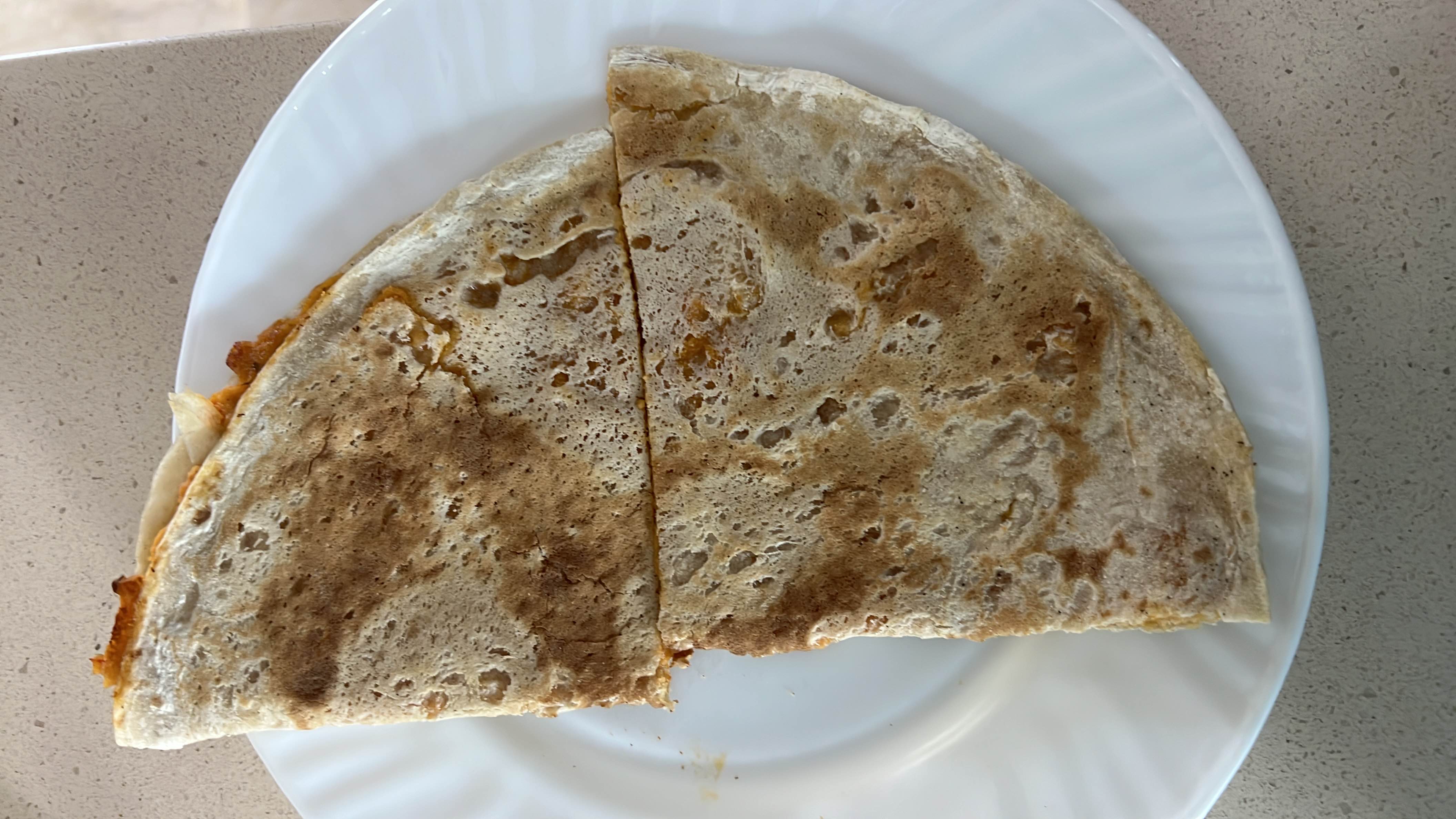 A grilled quesadilla with a crispy tortilla exterior, filled with melted cheese and sauce, providing a balanced mix of protein, carbs, and fats.