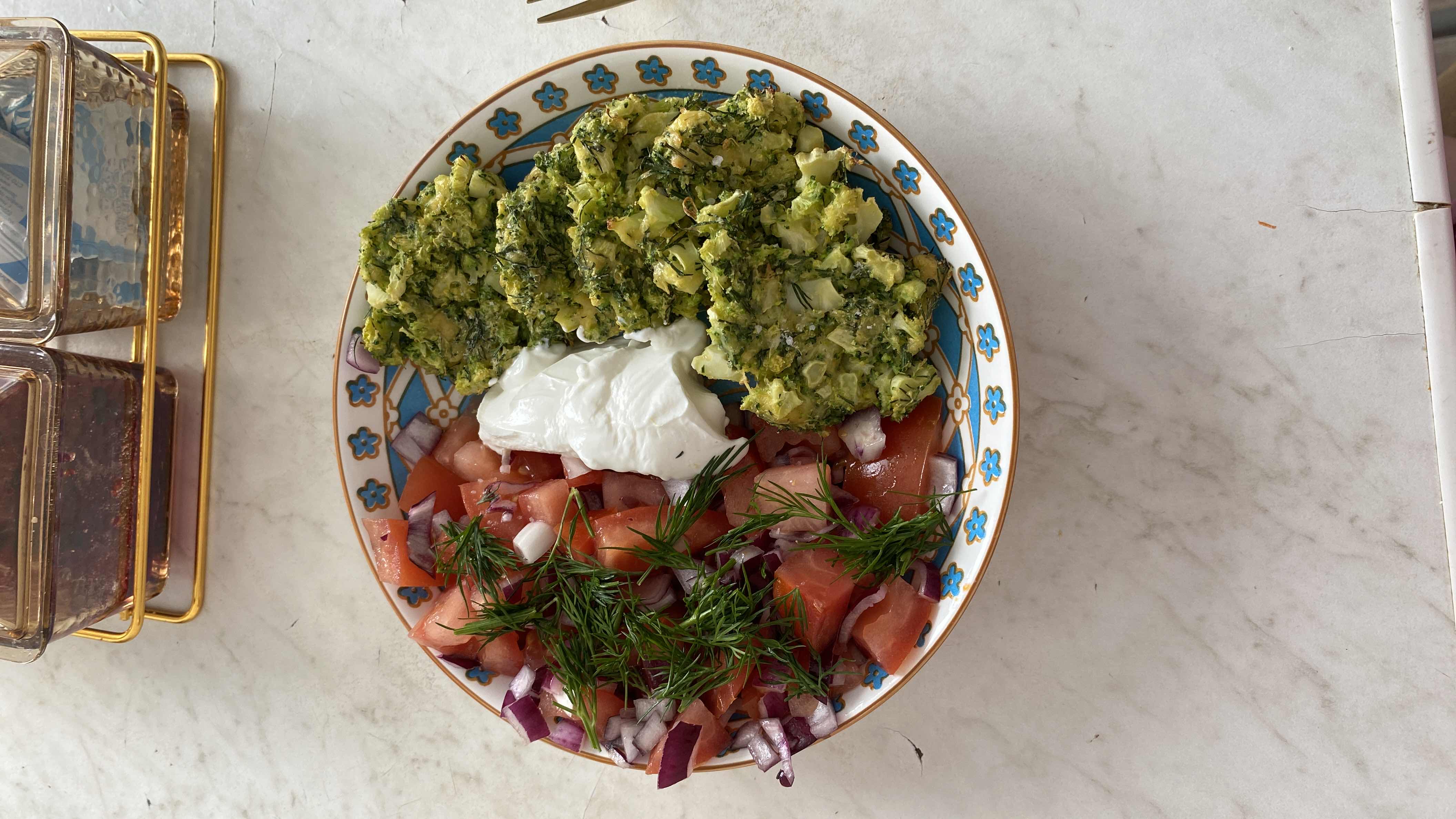 A nutritious meal consisting of broccoli fritters, fresh tomato and red onion salad with dill, and a side of Greek yogurt.