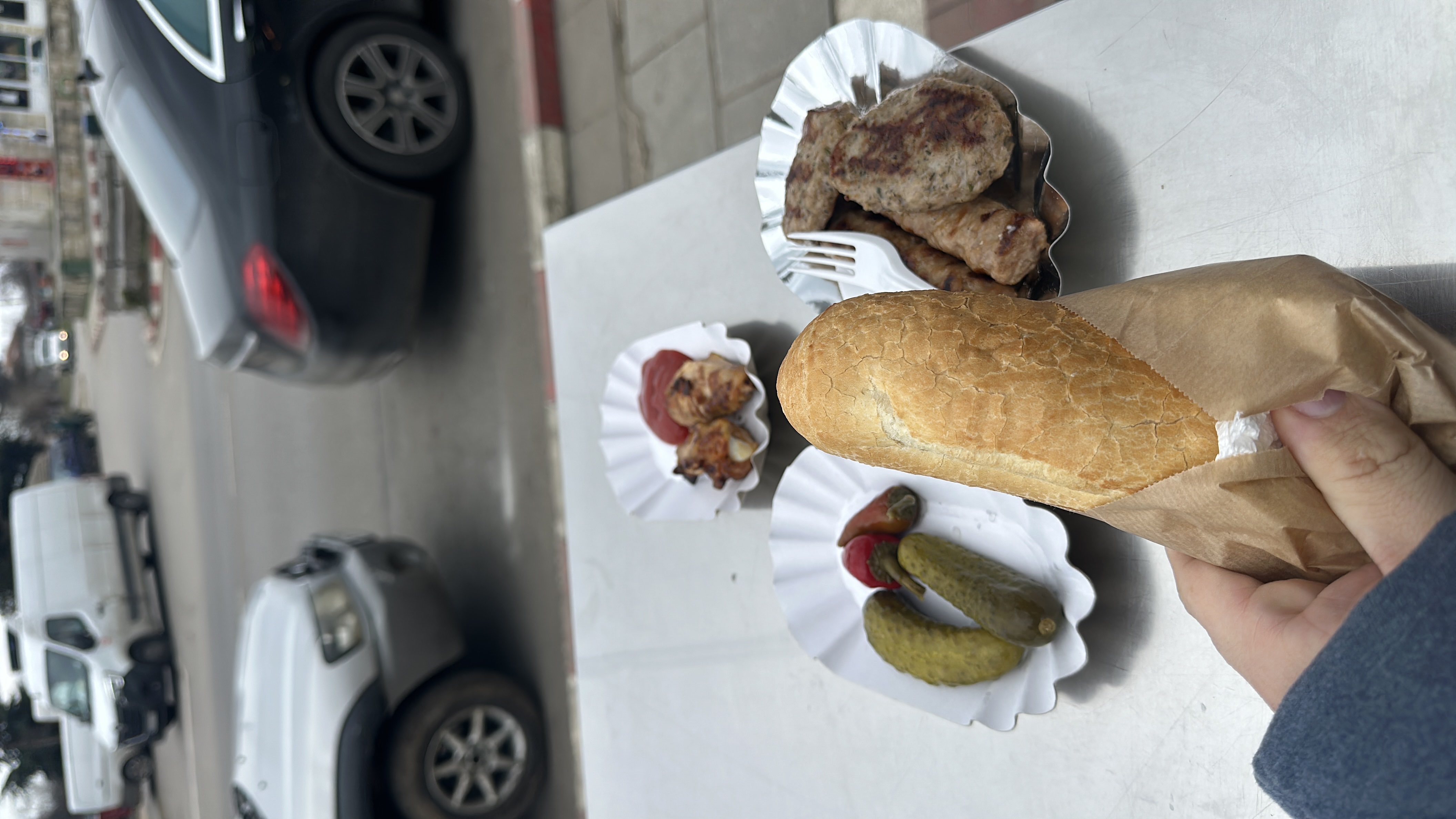 A meal consisting of bread, grilled meat, pickles, and bacon-wrapped meat, served with condiments.