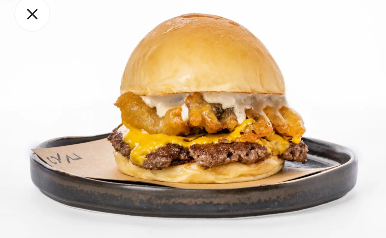 A high-calorie cheeseburger with a beef patty, melted cheese, crispy fried onion rings, and a creamy sauce, served in a soft bun.