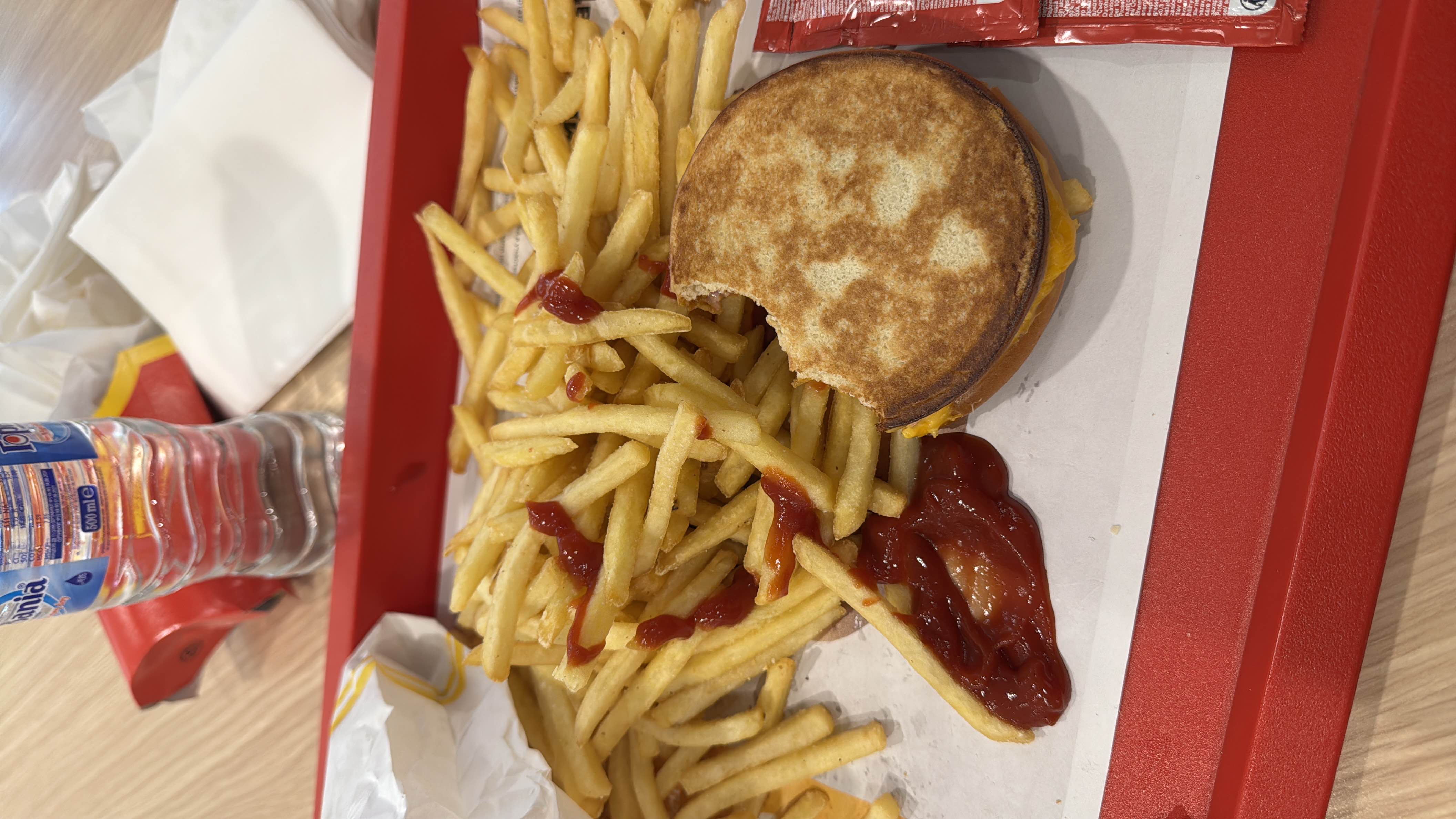 A fast food meal consisting of French fries with ketchup and a cheeseburger, high in calories and fats with moderate protein content.