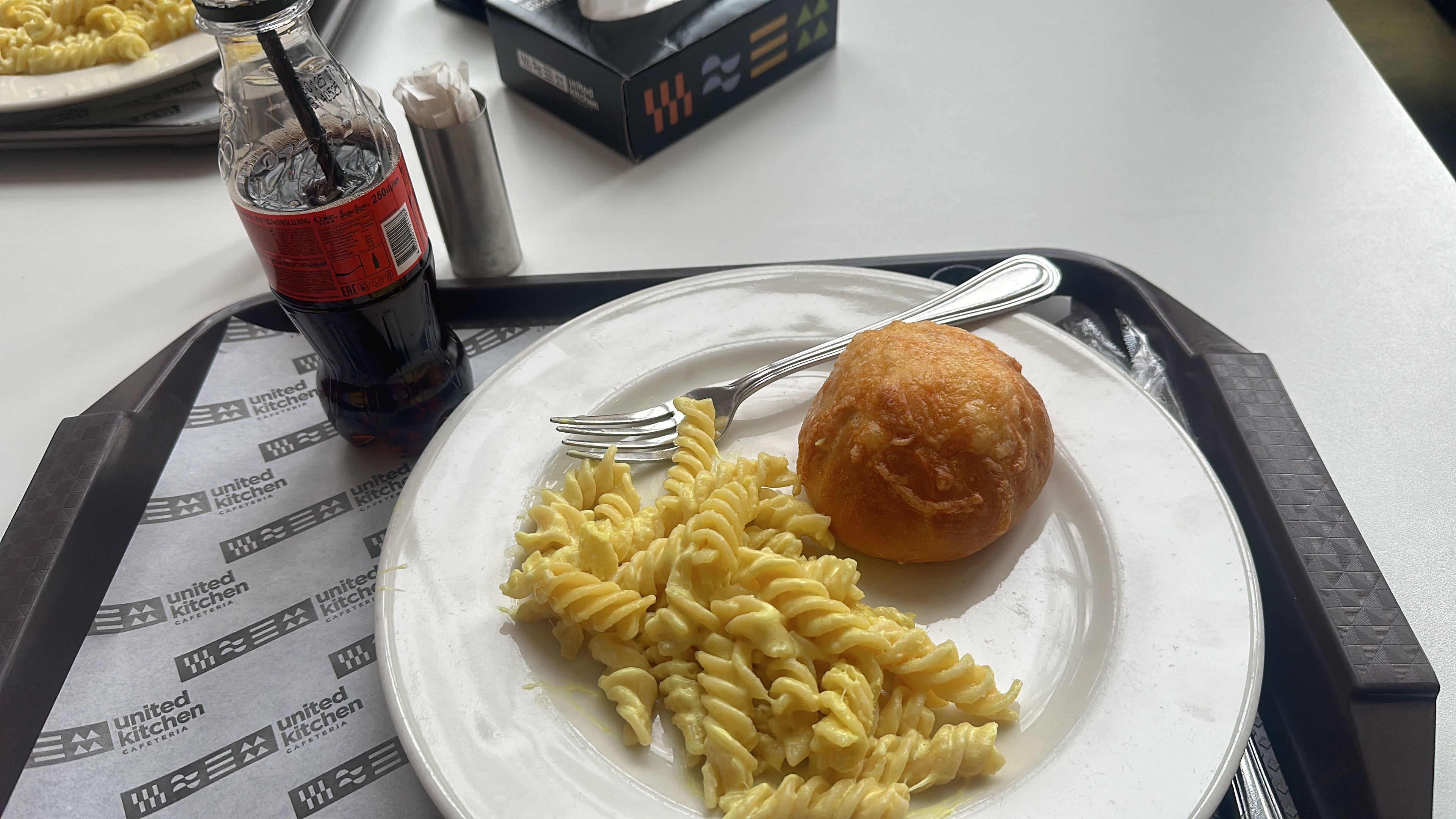 A meal consisting of creamy cheese pasta, a bread roll, and a cola drink, providing a moderate balance of carbohydrates, fats, and protein.