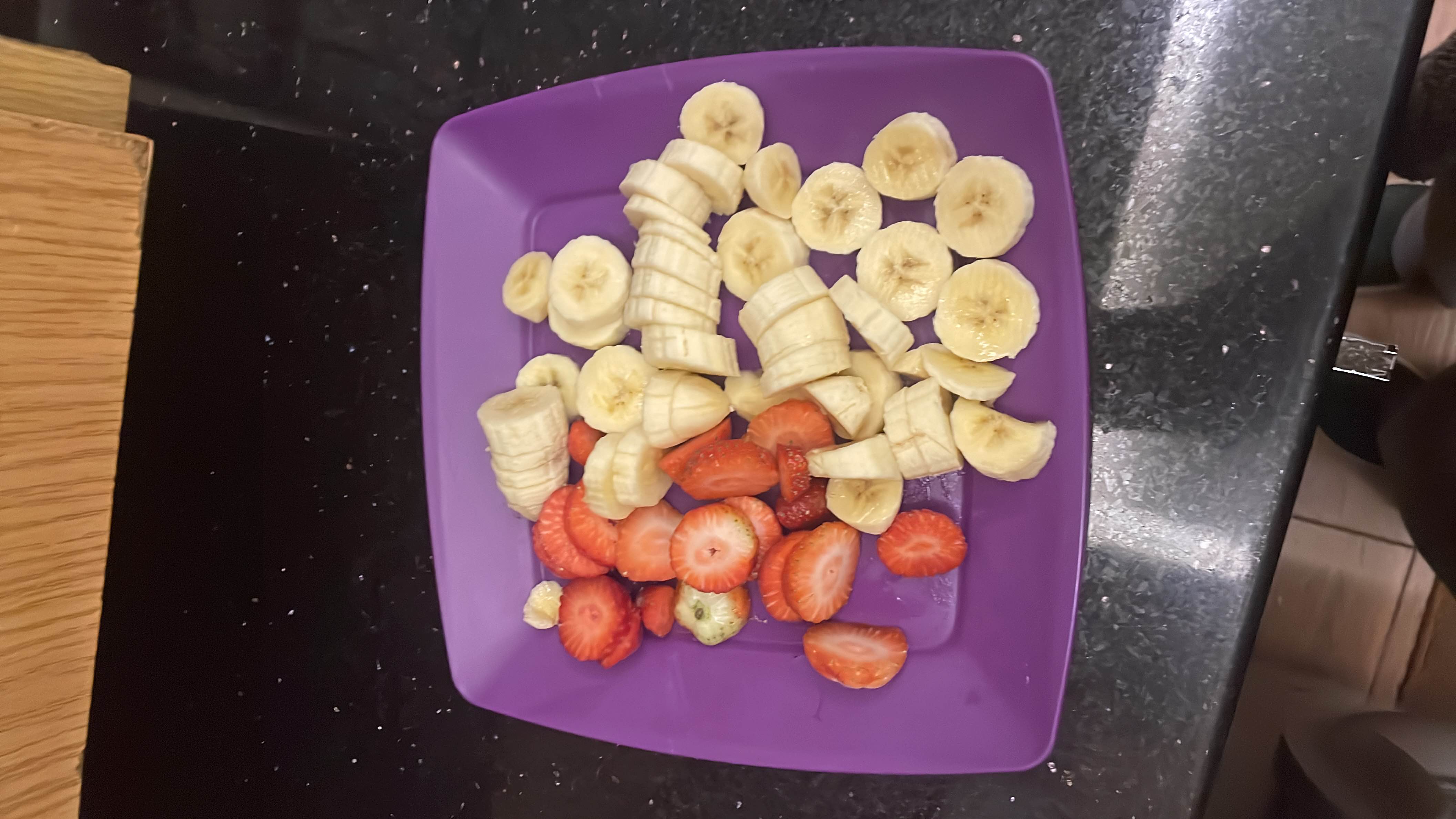 A plate of sliced bananas and strawberries, providing a healthy and nutritious snack rich in carbohydrates and vitamins.