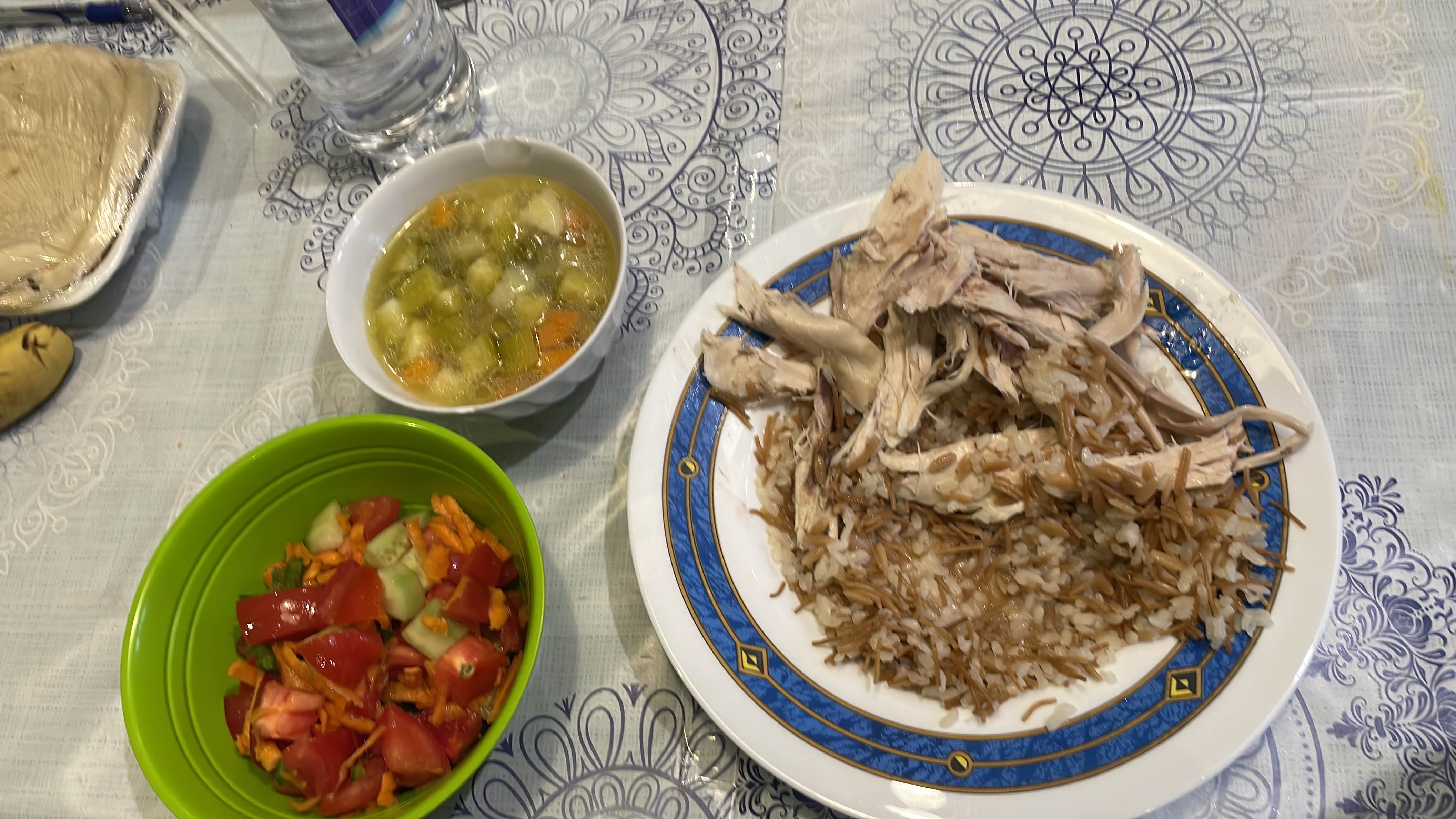 A balanced meal consisting of shredded chicken, rice with vermicelli, vegetable soup, and a fresh salad.