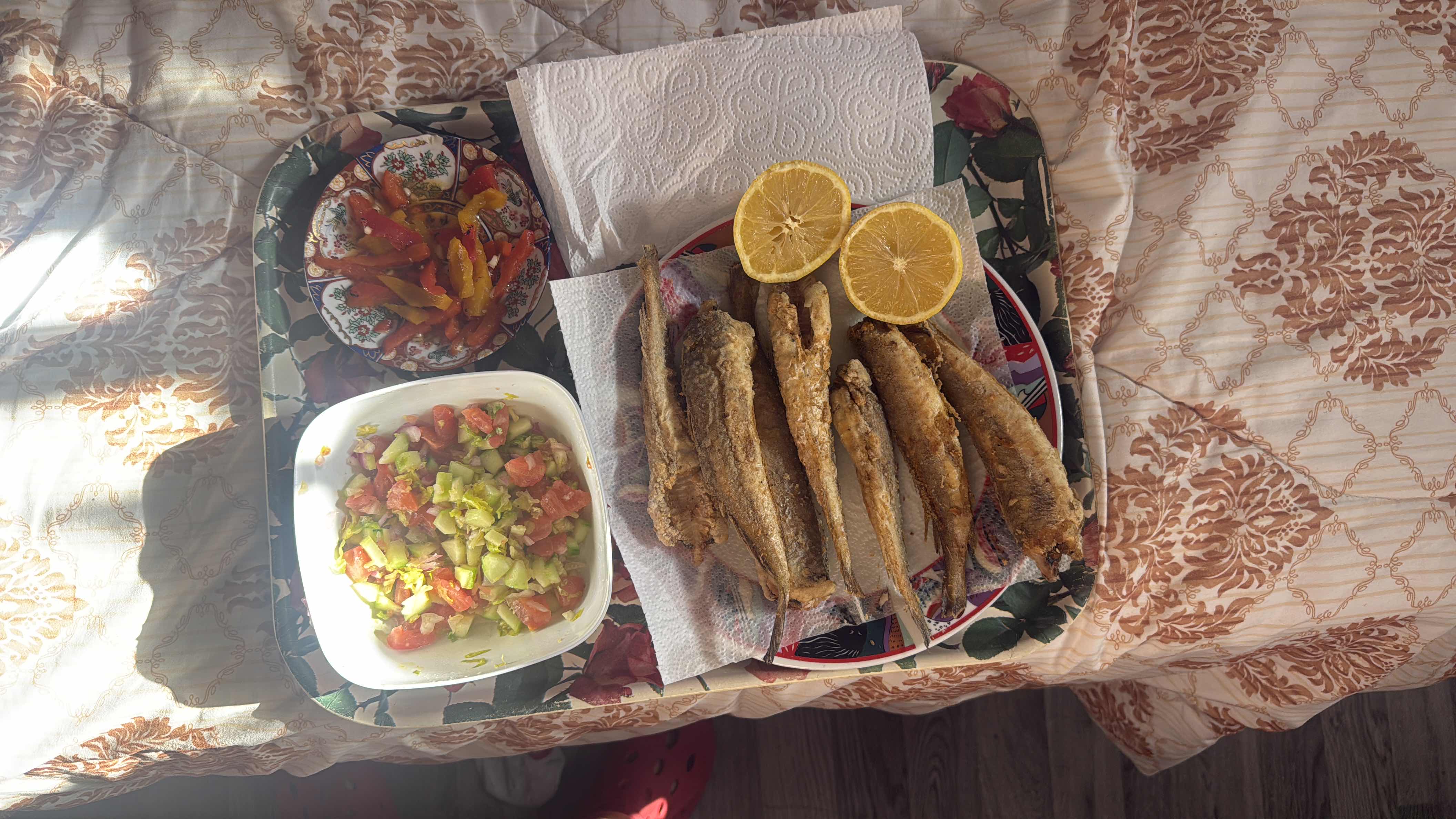 A balanced meal consisting of fried fish, fresh vegetable salad, and grilled bell peppers, served with lemon for added flavor.