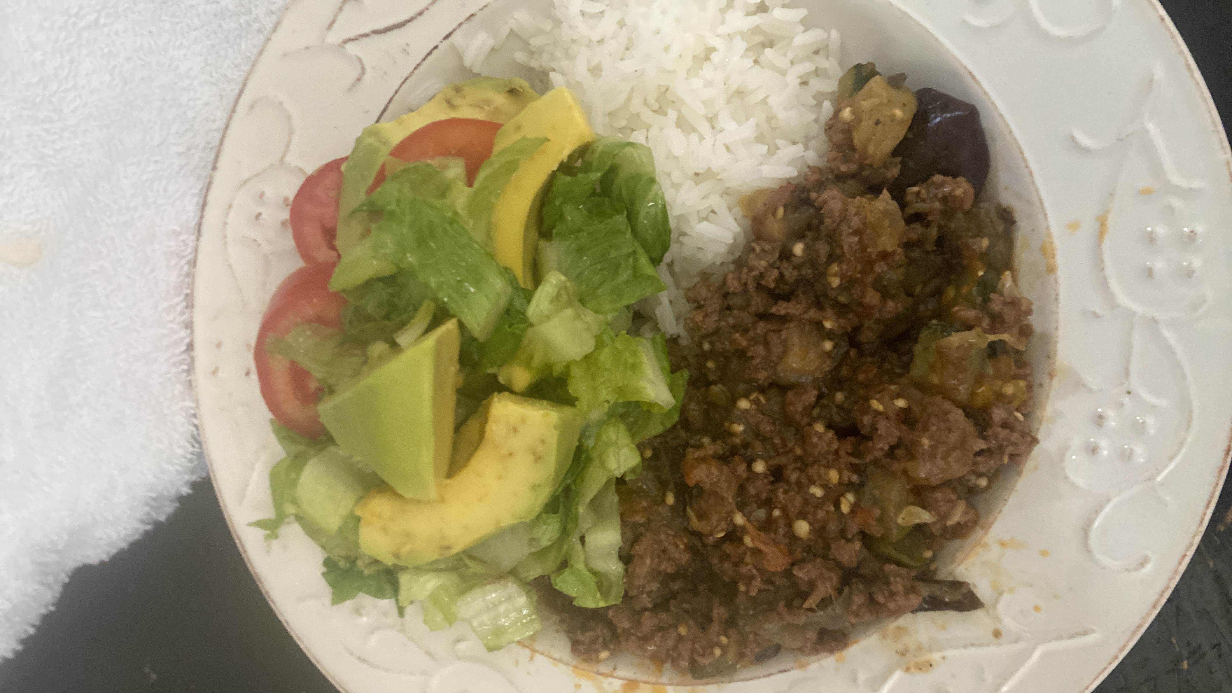 A balanced meal consisting of seasoned ground beef, white rice, and a fresh salad with avocado, lettuce, and tomato.