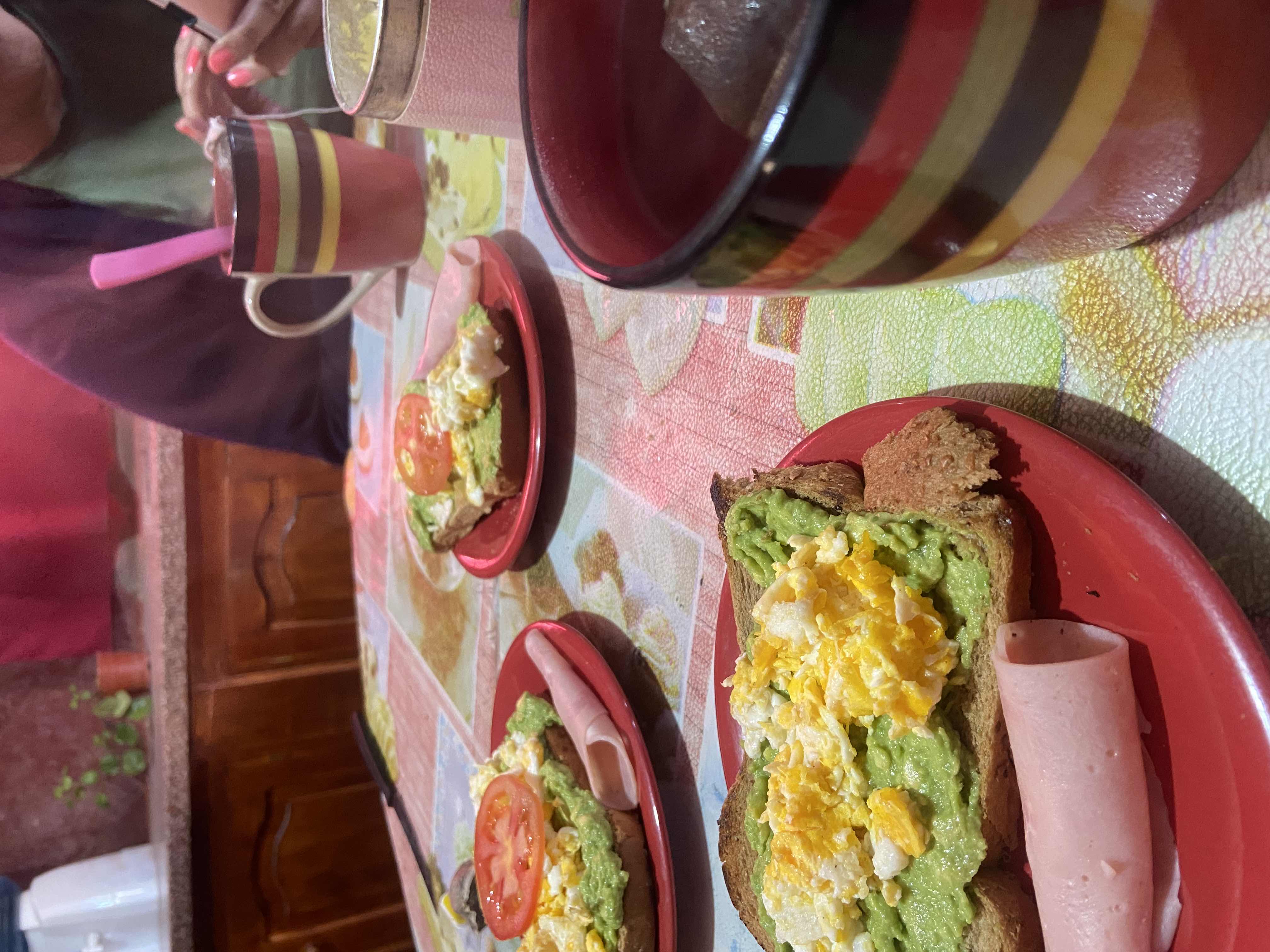 A balanced breakfast featuring avocado toast with scrambled eggs, a slice of ham, and a hot beverage.