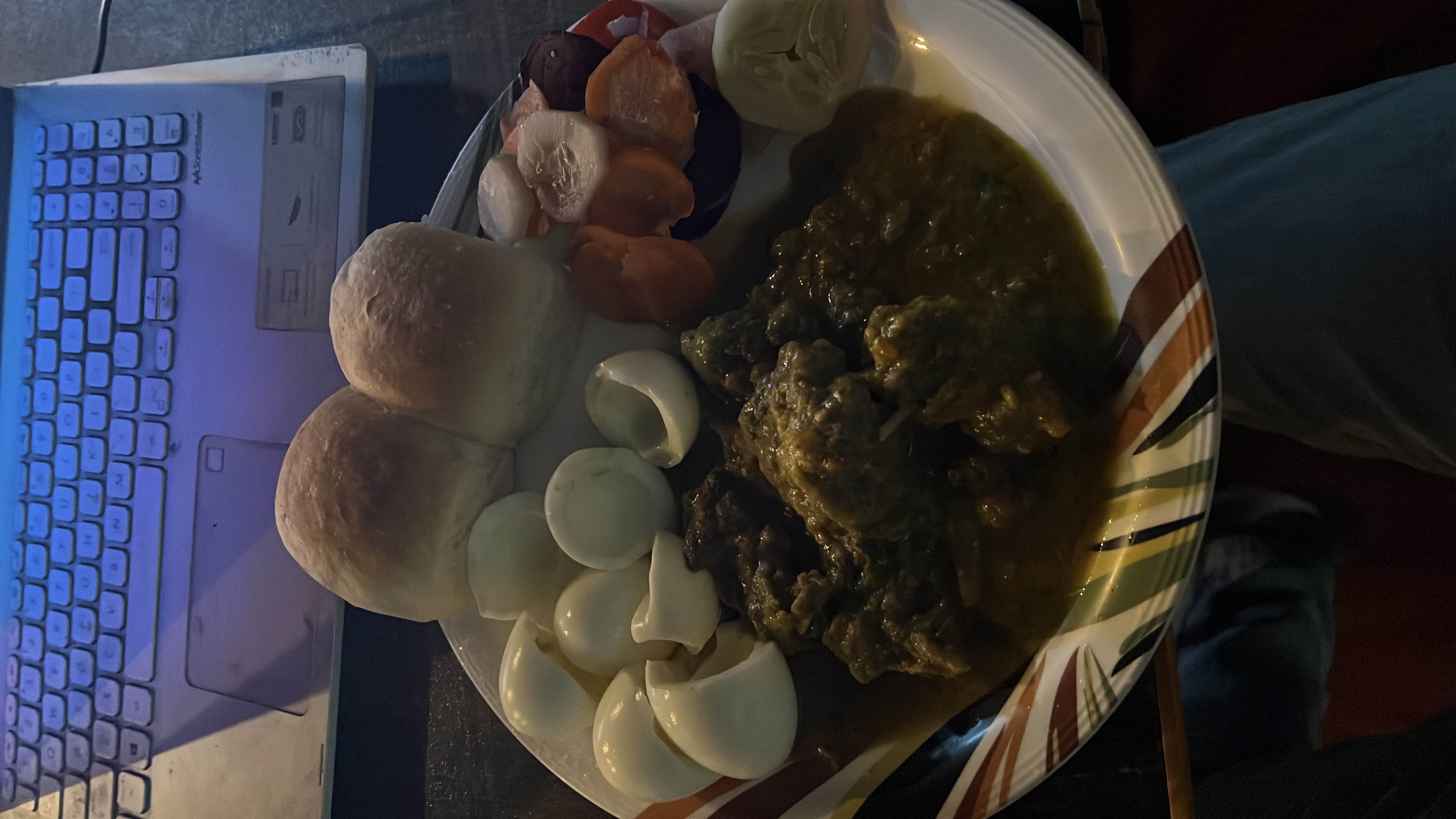 A balanced meal consisting of boiled eggs, bread rolls, vegetable curry, and sliced vegetables.